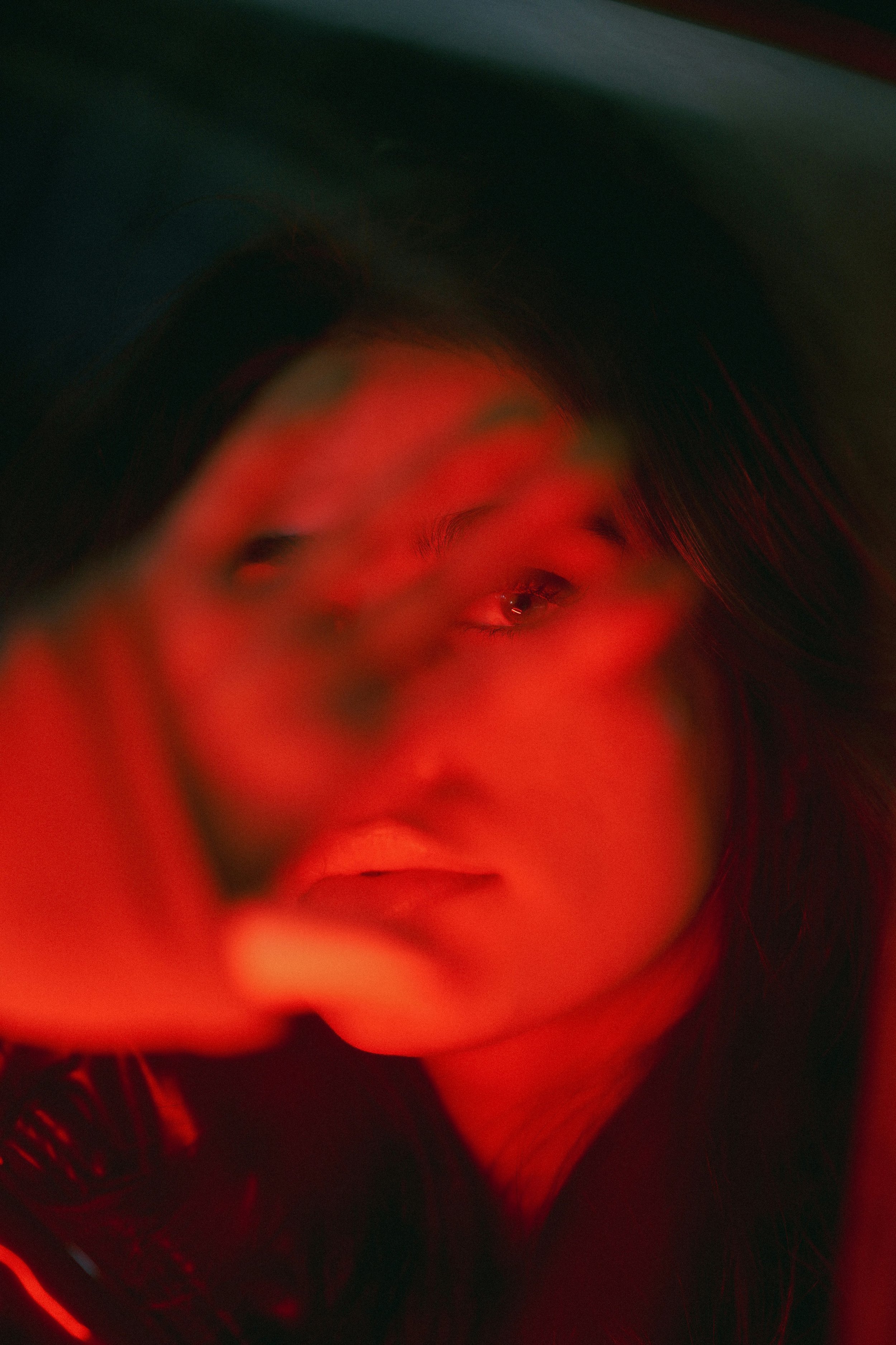Woman holding hand in front of face. Glowing with deep red light. Moody.