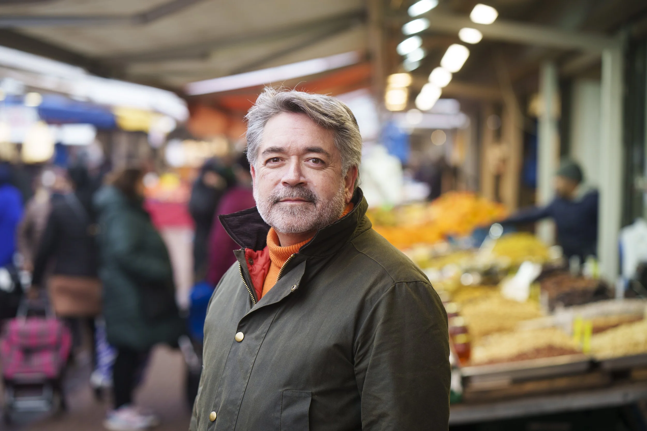 Andrew van Esch die buiten op een markt staat, omgeven door mensen en fruitkramen.
