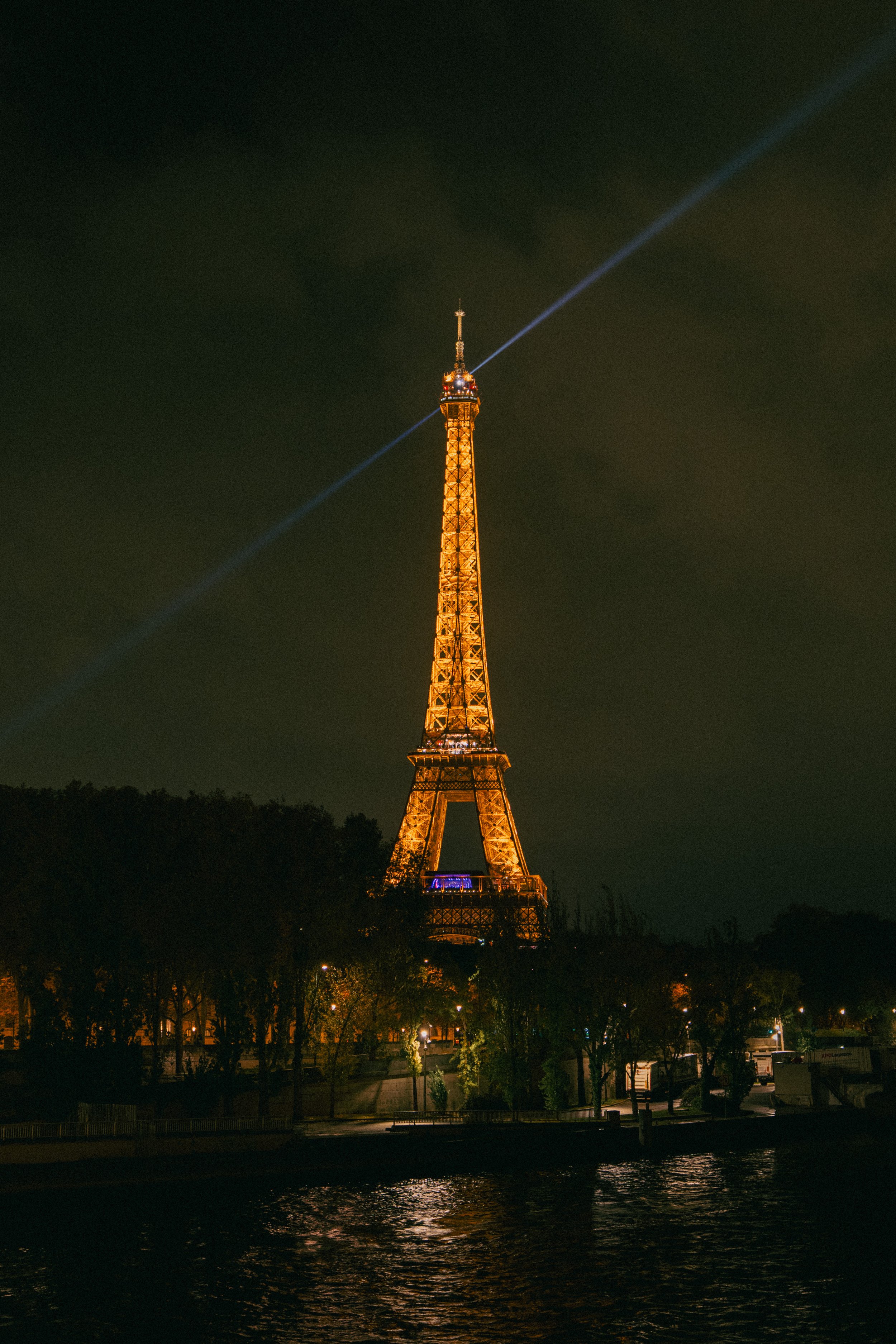 The Eiffel Tower illuminated at night with a spotlight beam extending from the top.
