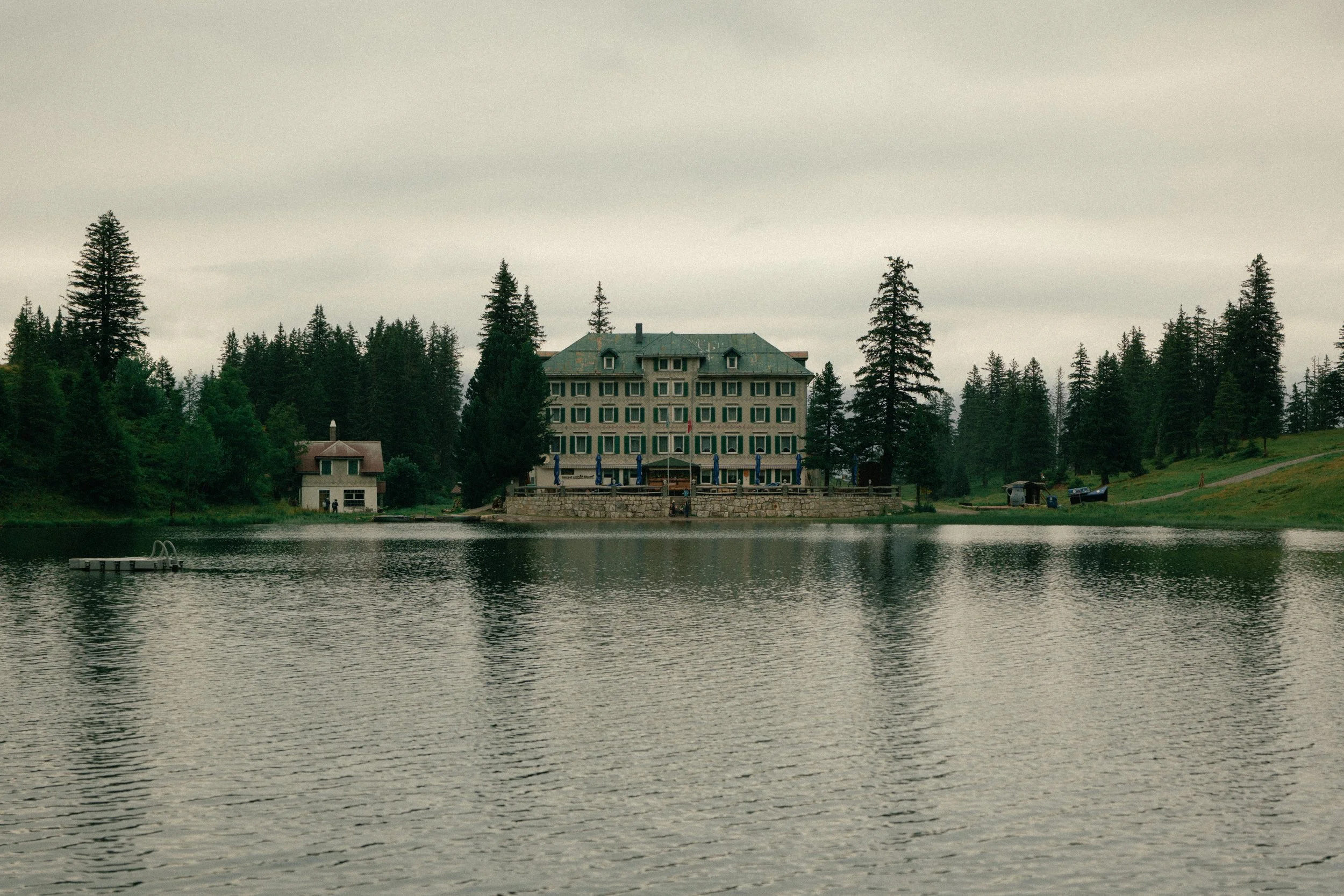 A large hotel overlooking a lake, with trees surrounding the area and a cloudy sky.