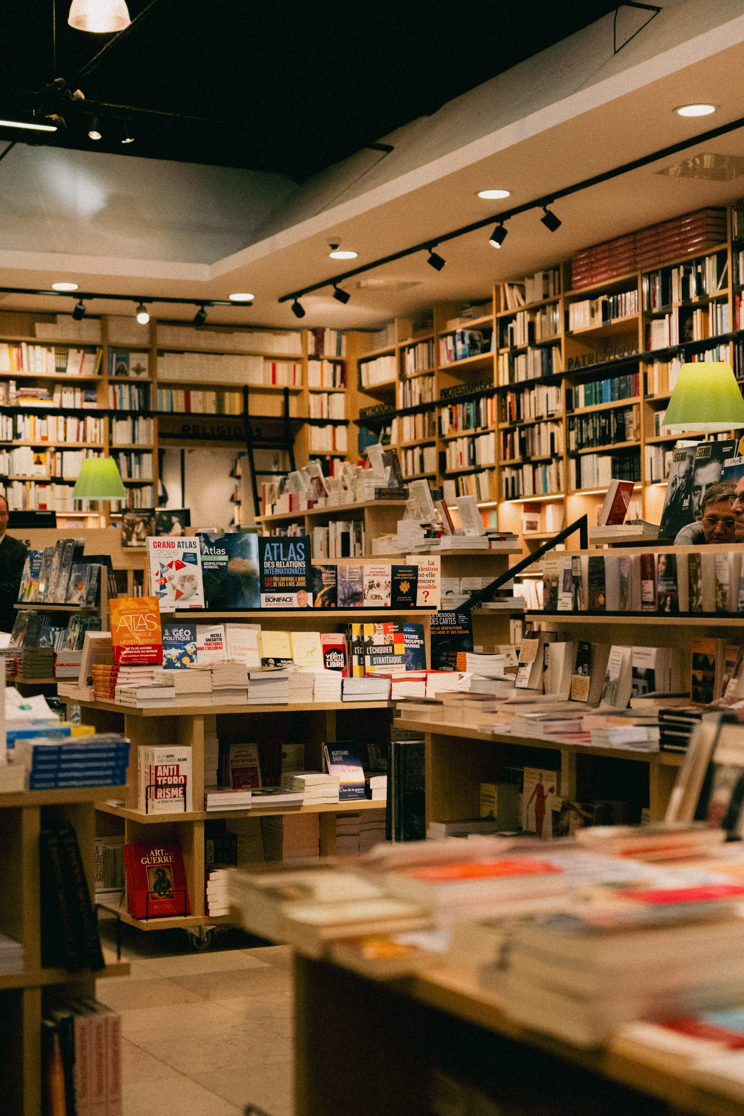 Interior of a bookstore with shelves filled with books, tables displaying more books, and warm ambient lighting.