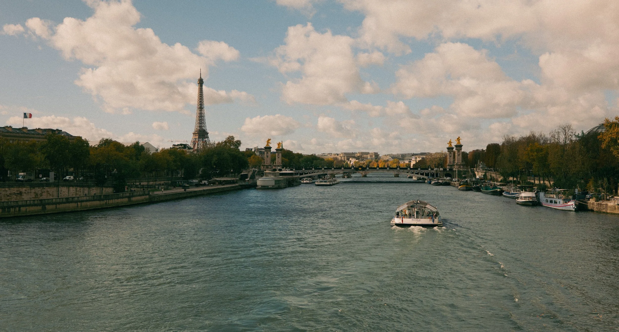A river with boats, the Eiffel Tower in the background, and cloudy sky.