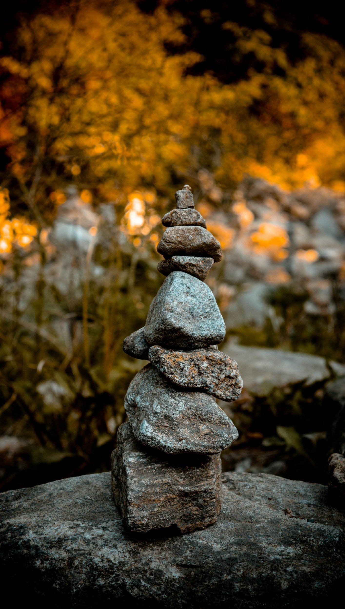 A stack of various-sized rocks balanced on top of each other outdoors during autumn with blurred orange leaves in the background.