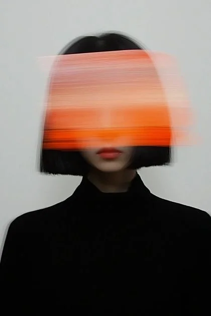 A person with black hair in a bob haircut wearing a black turtleneck, with a blurred orange and pink streak covering their face against a plain white background.