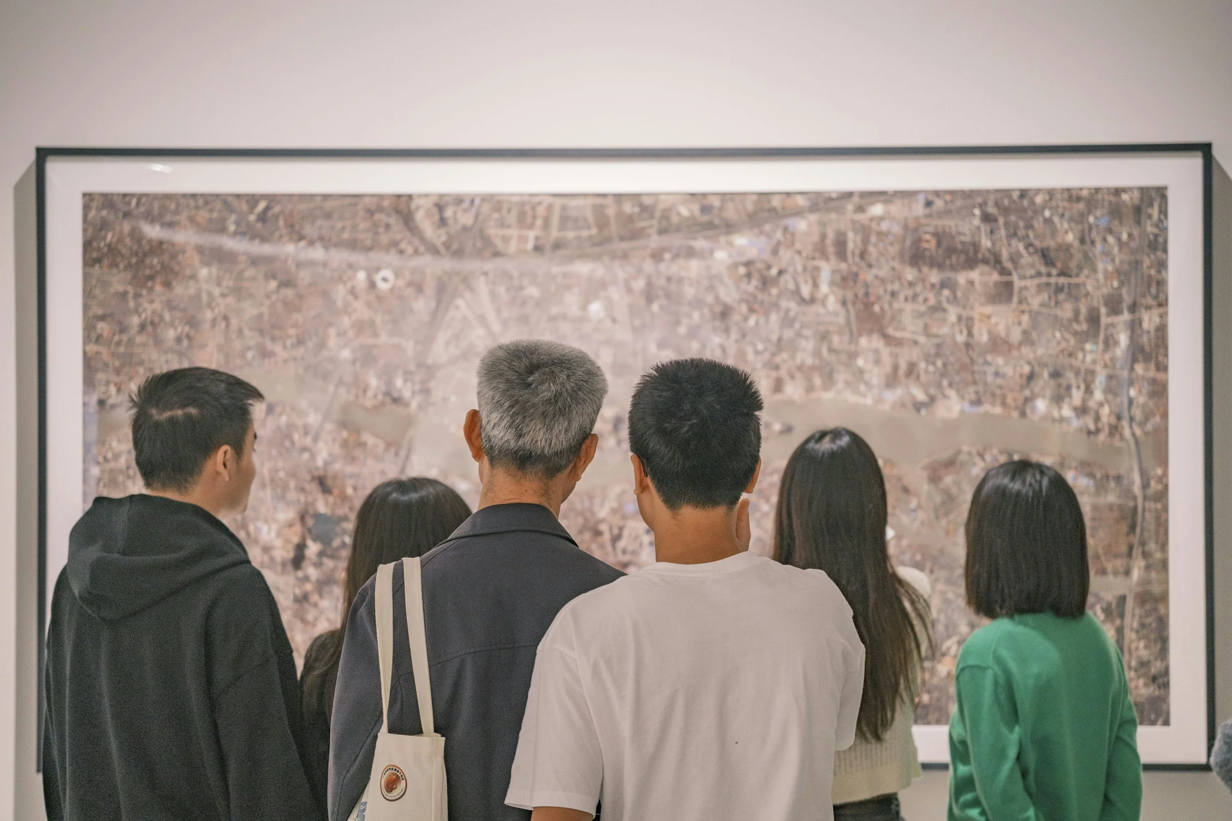 Group of people standing in front of a large wall map in an art gallery or museum.