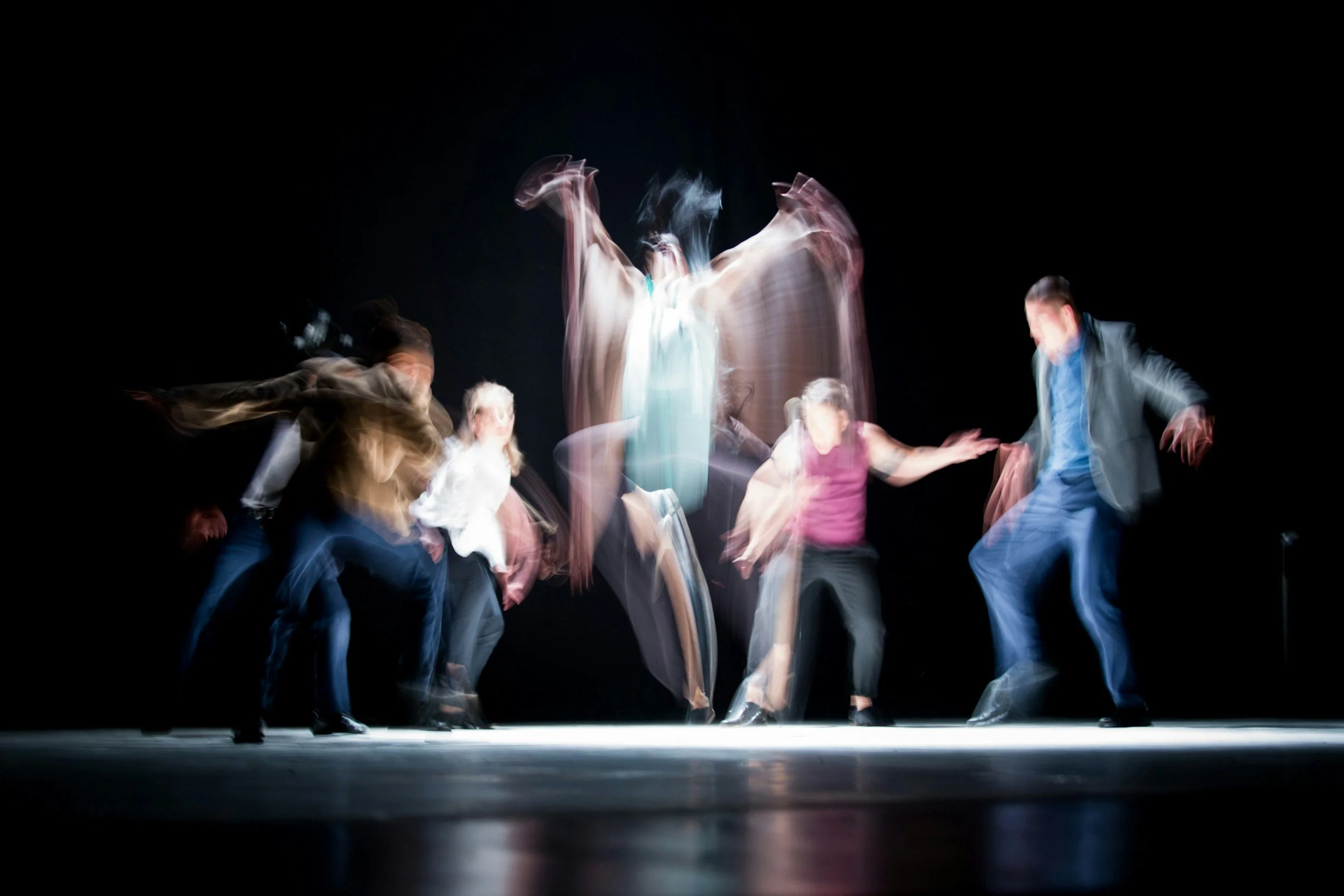 Dancers performing on a dark stage, motion-blurred to show movement and energy.