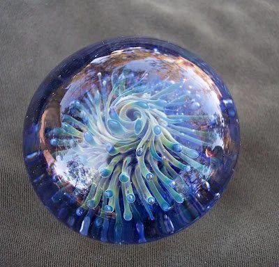 Colorful glass paperweight with a spiral design, resting on a gray fabric surface.