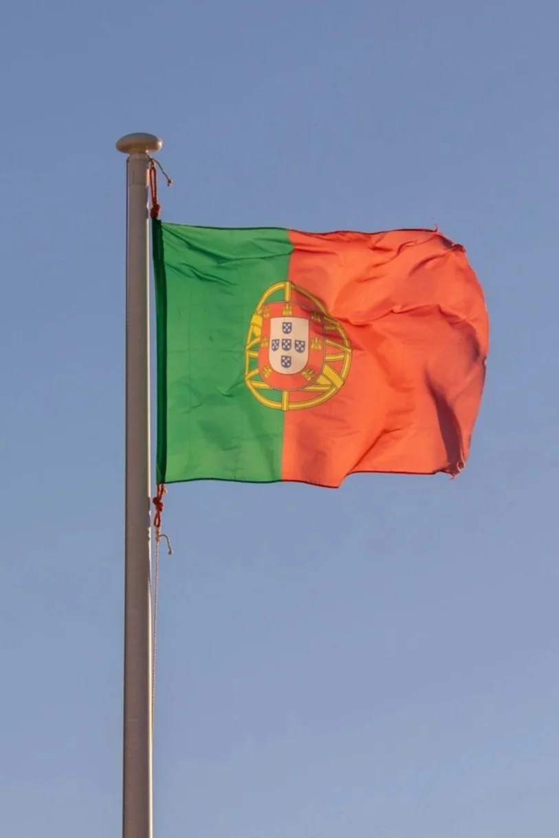 Portuguese flag waving in the wind against a blue sky.