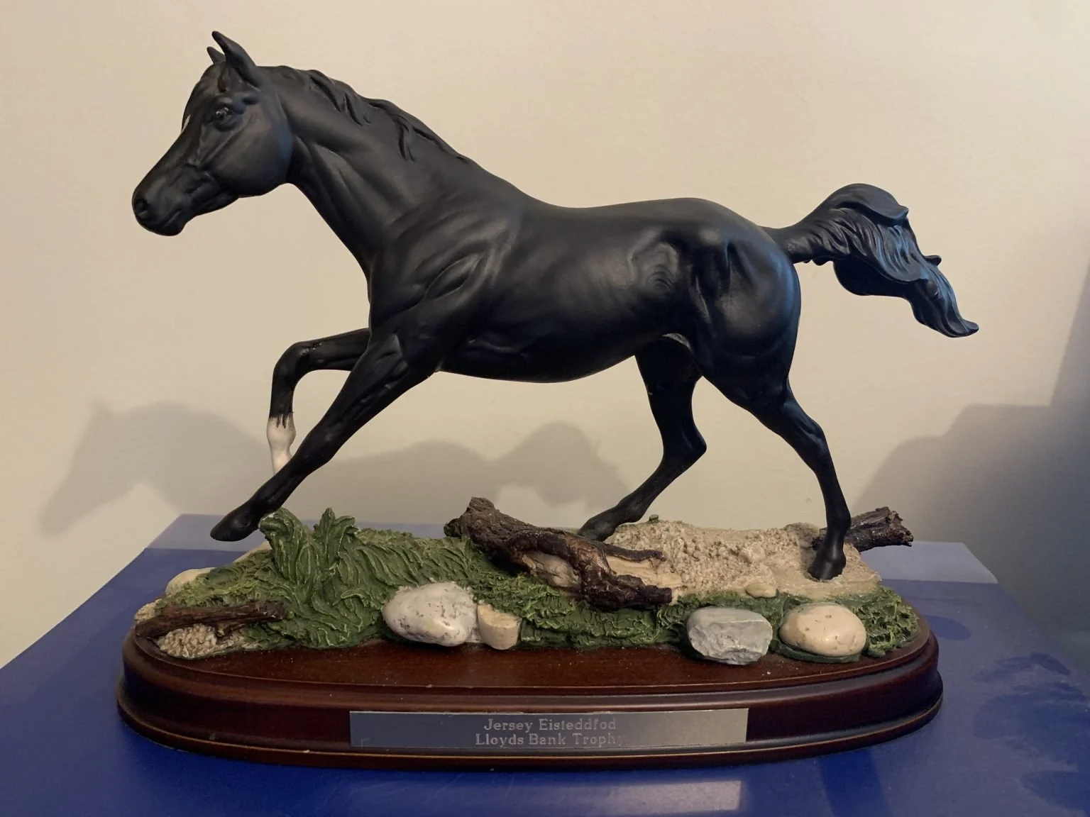A black horse sculpture in a running pose on a base with rocks and greenery.