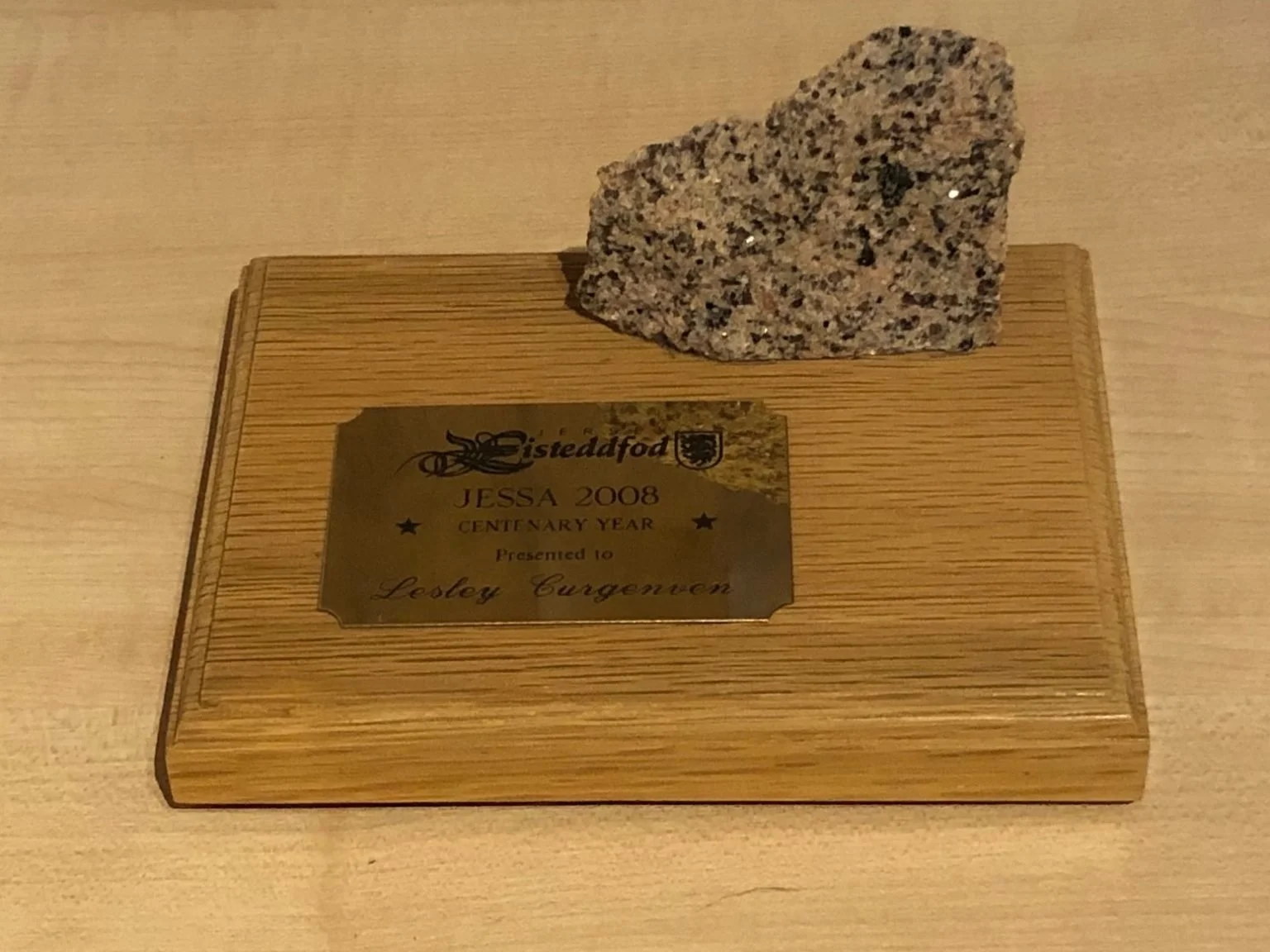 A wooden box with a metallic plaque and a granite rock on top. The plaque reads: 'sistedafod JESSA 2008 CENTENARY YEAR Presented to Lestey Curgwen' with decorative elements.