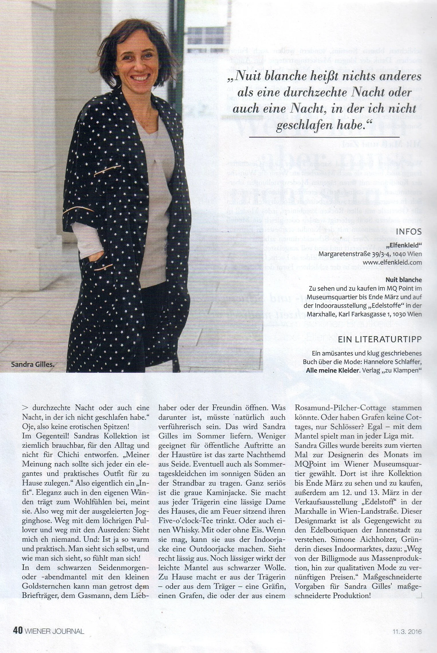 Eine Frau mit dunklen, lockigen Haaren trägt einen schwarzen Mantel mit weißen Sternen, steht in einem hellen Raum, lächelt und schaut zur Kamera.