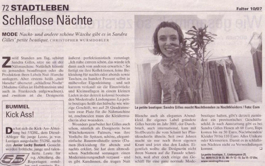 Schwarz-weiß Fotografie einer Frau, die neben einem Kleiderständer mit Nachthemden steht, in einem Modegeschäft.