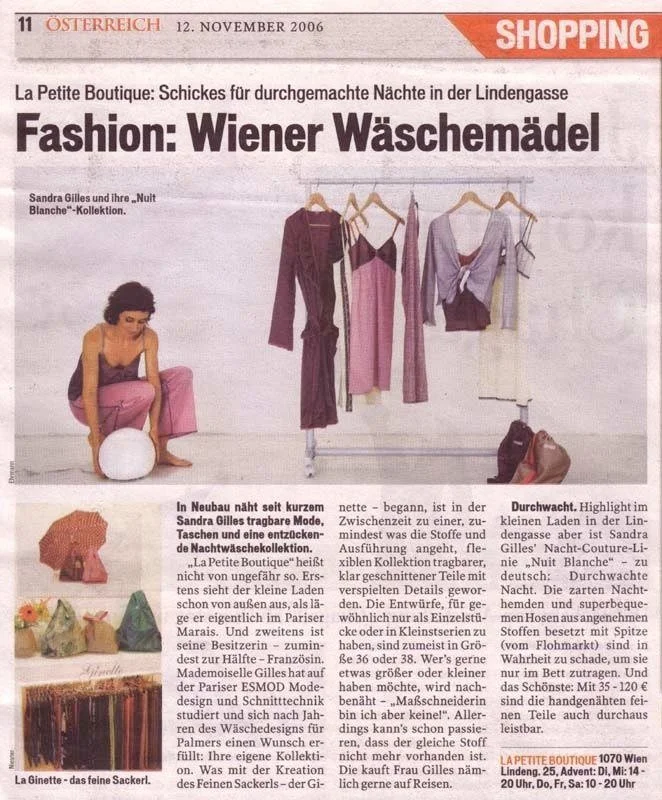 Ein Zeitungsfoto zeigt eine Frau, die auf dem Boden sitzt, umgeben von Kleiderstangen mit Damenmode und Taschen. Im Hintergrund sind Kleidungsstücke aufgehängt, darunter ein pinkes Kleid, eine lila Jacke und andere Outfits. Mehrere Taschen liegen auf