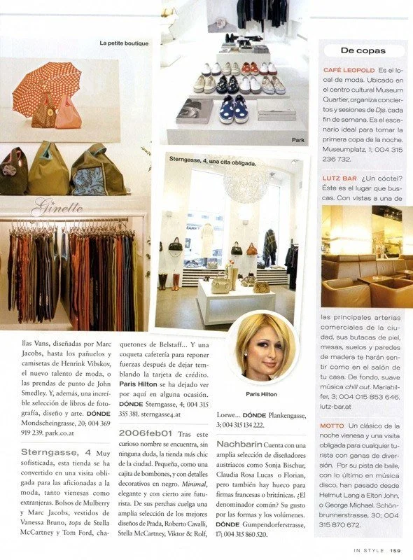 Ein Foto zeigt verschiedene Geschäfte und Schaufenster eines Einkaufsviertels mit Schuhen, Kleidung, Taschen und Möbeln. Es gibt Texttafeln mit Beschreibungen und Preisen, darunter eine Boutique, ein Schuhgeschäft, ein Kleidungsgeschäft, ein Café und