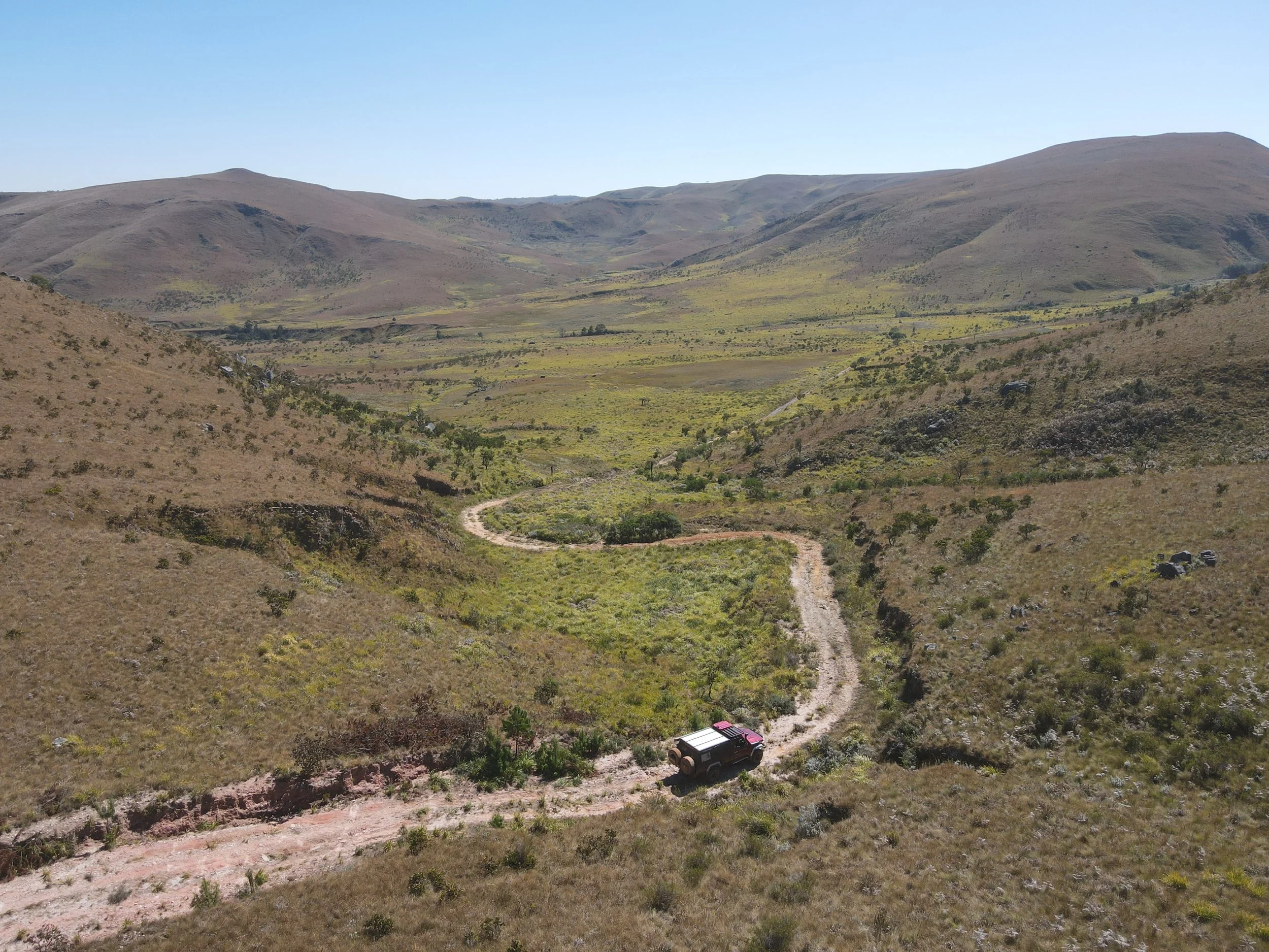 A drone image of Mt. Nyangani in Zimbabwe. Green rolling hills with an off road track and a Land Cruiser driving through.