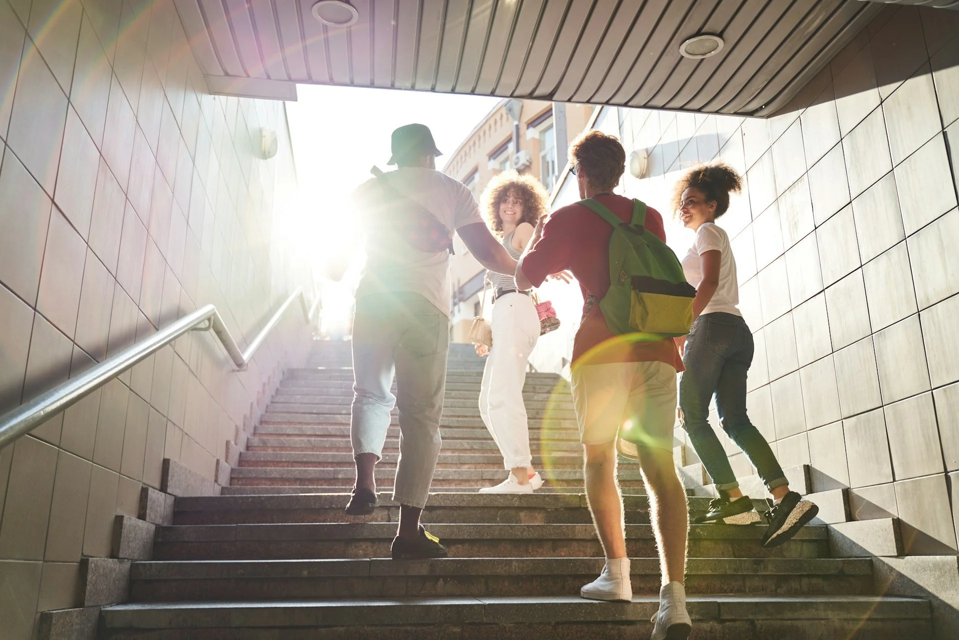 A group of five young people walking up outdoor city stairs, backlit by bright sunlight.