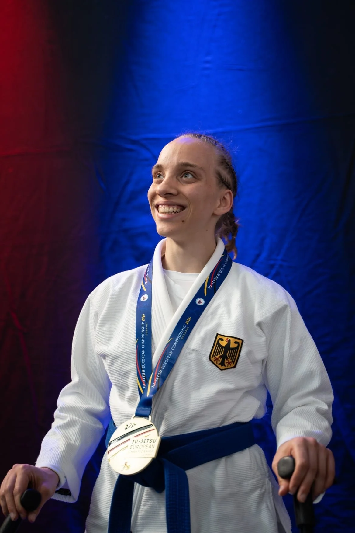 Junger weiblicher Judo-Sportler mit Medaille in einem weißen Judogi mit Deutschland-Emblem bei einem Wettbewerb.