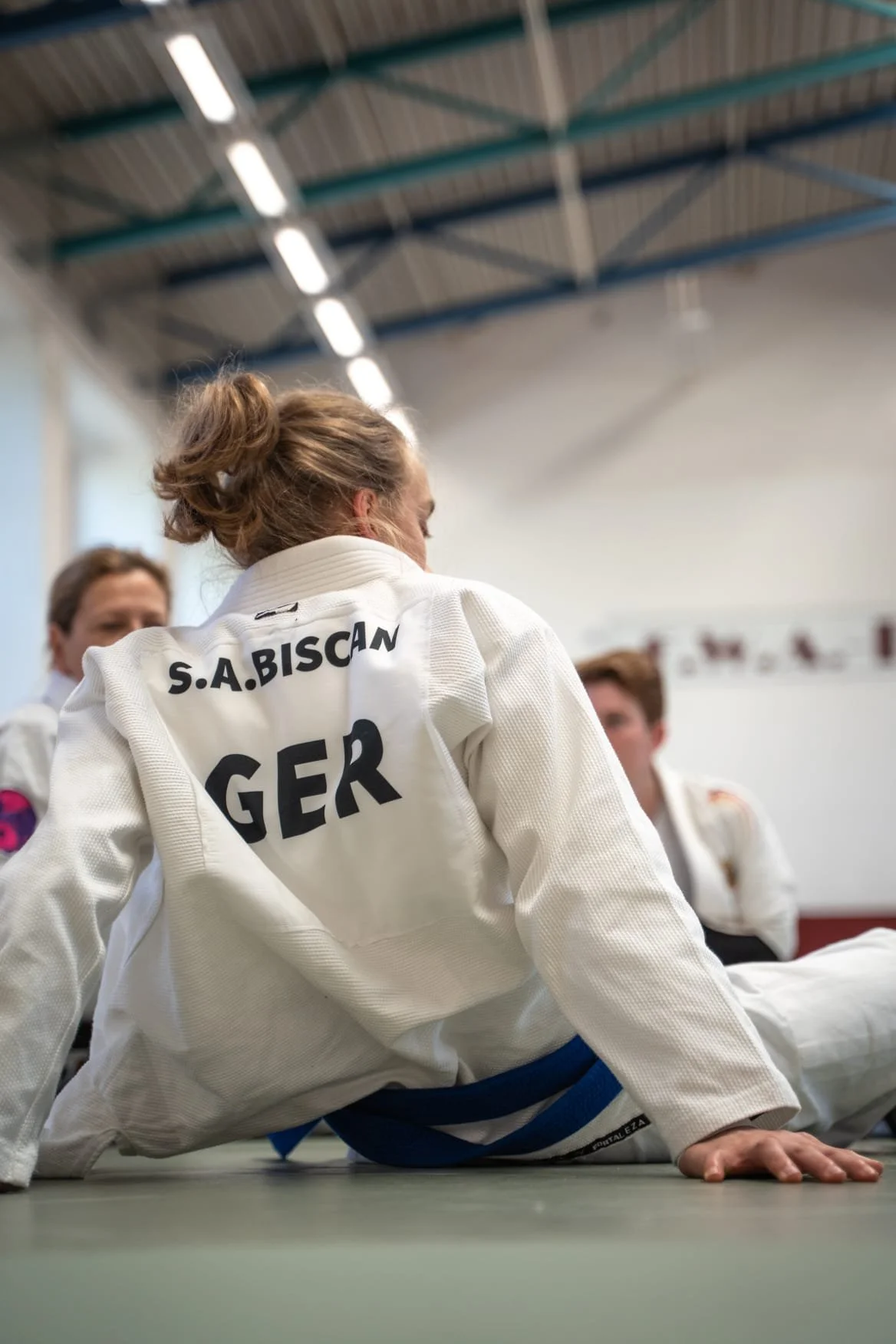 Junge Judo-Kämpferin im Gi mit Bundesfarben und Namen auf der Rückseite, im Judo-Trainingsraum