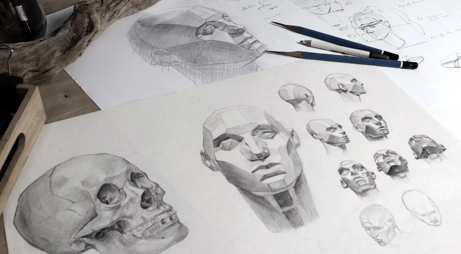 Sketches of human skulls and faces, some detailed and others in outline, with drawing tools and sketches of facial proportions on a desk.