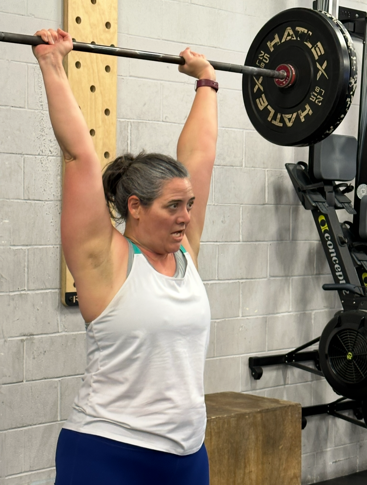 A woman lifting a barbell overhead during a workout at the gym.