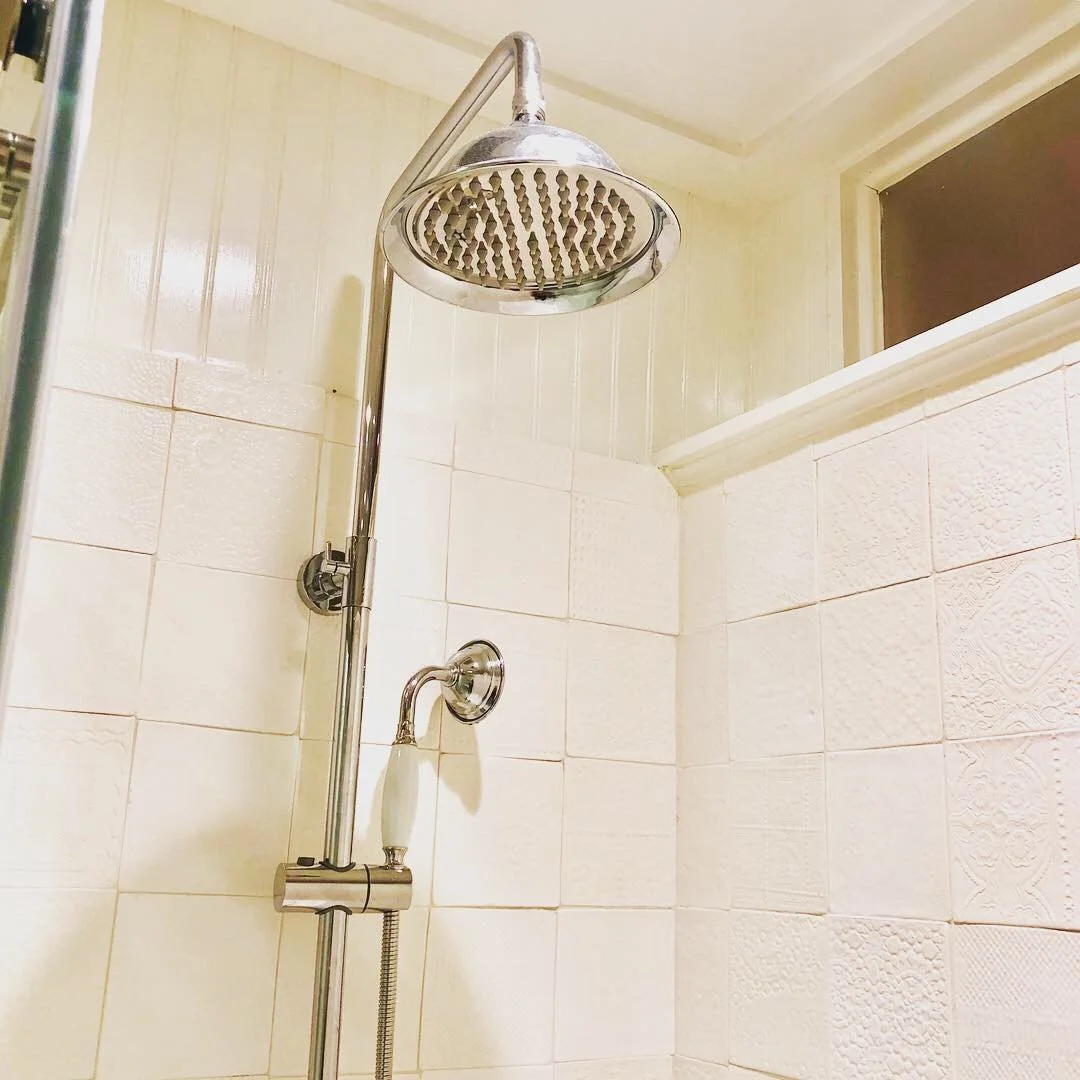 Close-up of a modern shower head with a handheld shower attachment on a tiled bathroom wall.