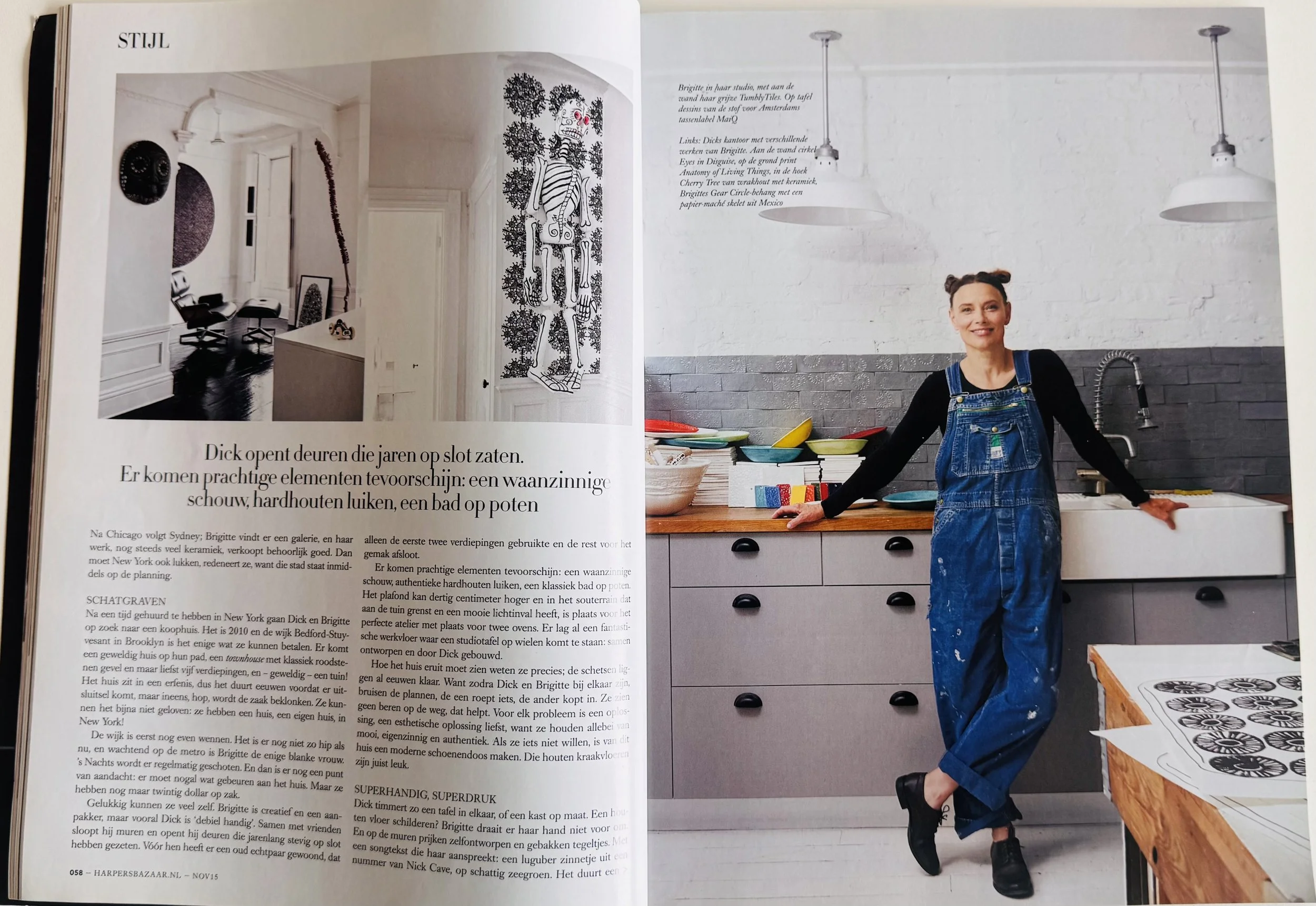 Open magazine spread featuring interior design and a woman in a kitchen. The left page shows a black and white photograph of a hallway with chairs and wall art. The right page displays a smiling woman with two buns in her hair, wearing blue overalls and a black shirt, standing in a modern kitchen with a white wall, gray tile backsplash, and colorful bowls on a wooden countertop.