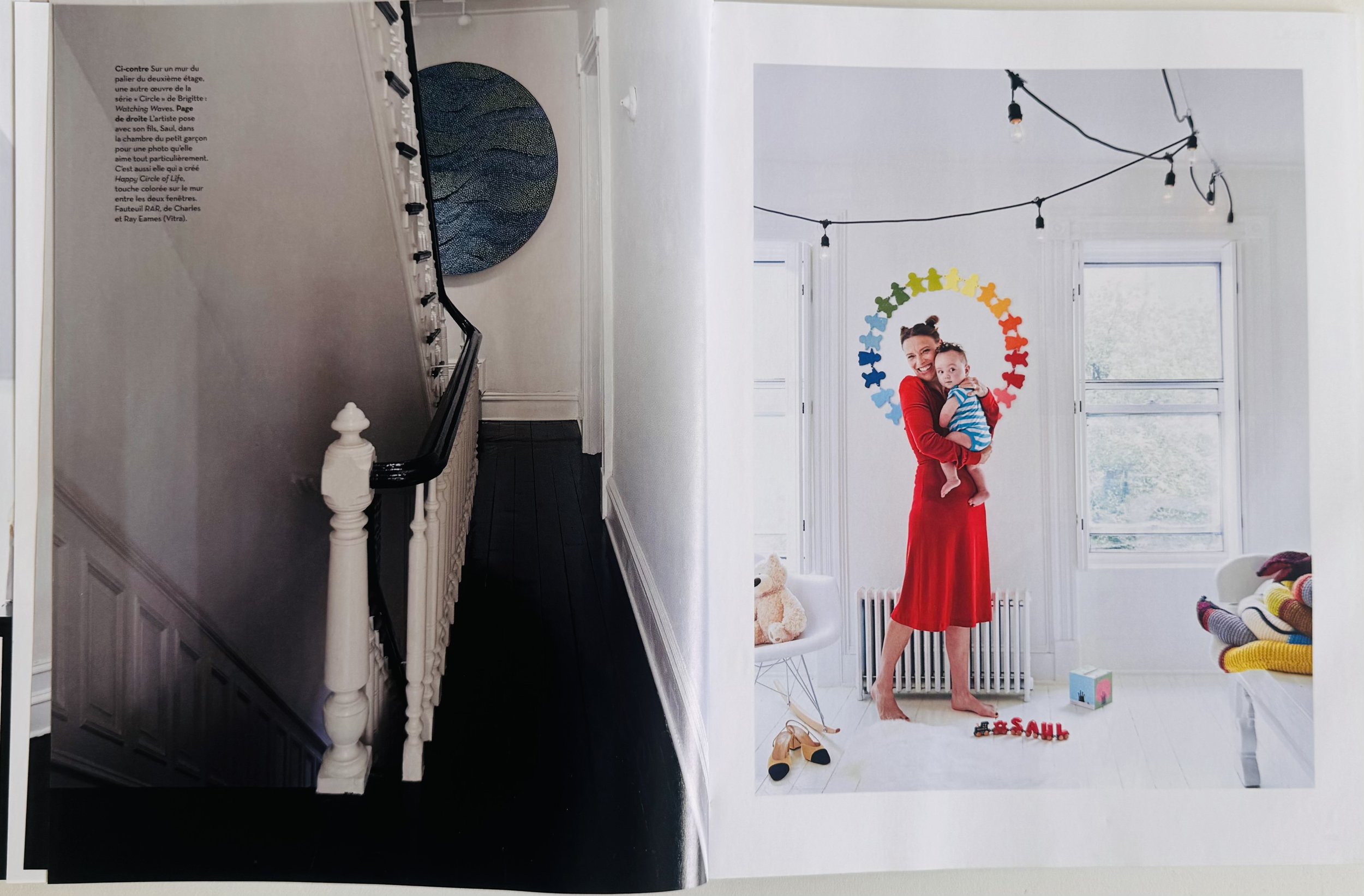 Interior of a house with a staircase on the left and a bright room on the right. The right room has a woman in a red dress holding a child, with colorful puzzles arranged in a circle above their heads, large windows, and various toys and decorations.