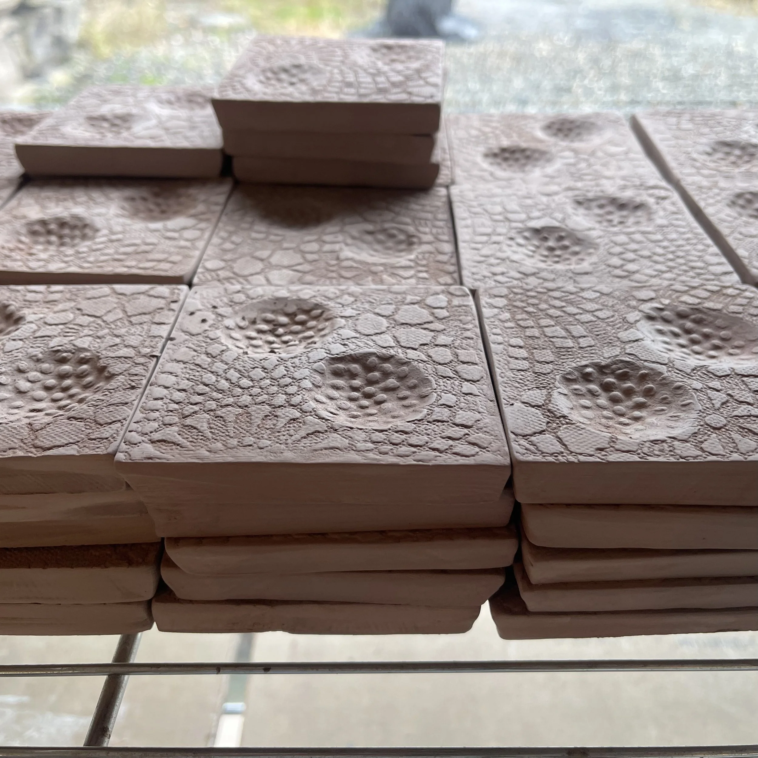 Stacked square ceramic tiles with textured surfaces resembling reptile or crocodile skin patterns, arranged neatly on a rack.