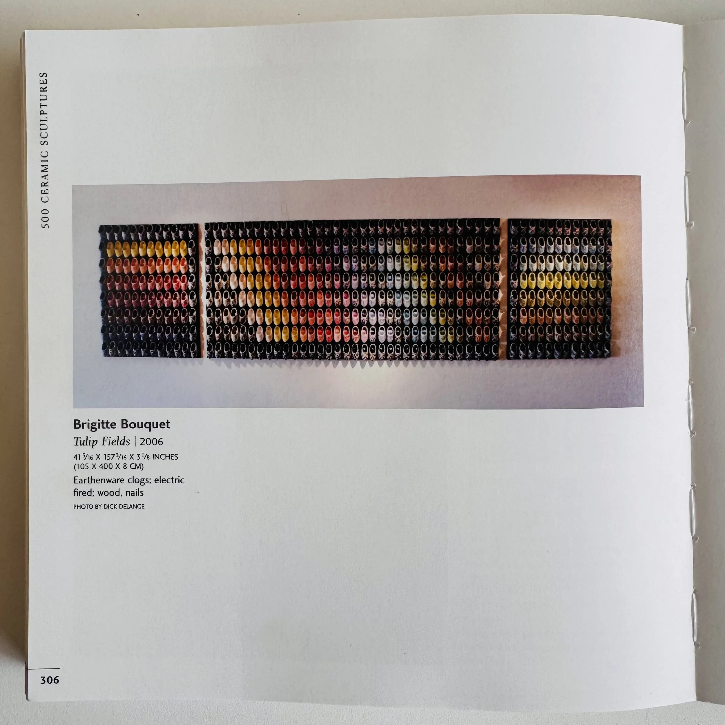 Photograph of an art piece titled 'Tulip Fields' by Brigitte Bouquet, created in 2006, consisting of numerous ceramic clogs arranged in three sections with colored glazes resembling a tulip field.