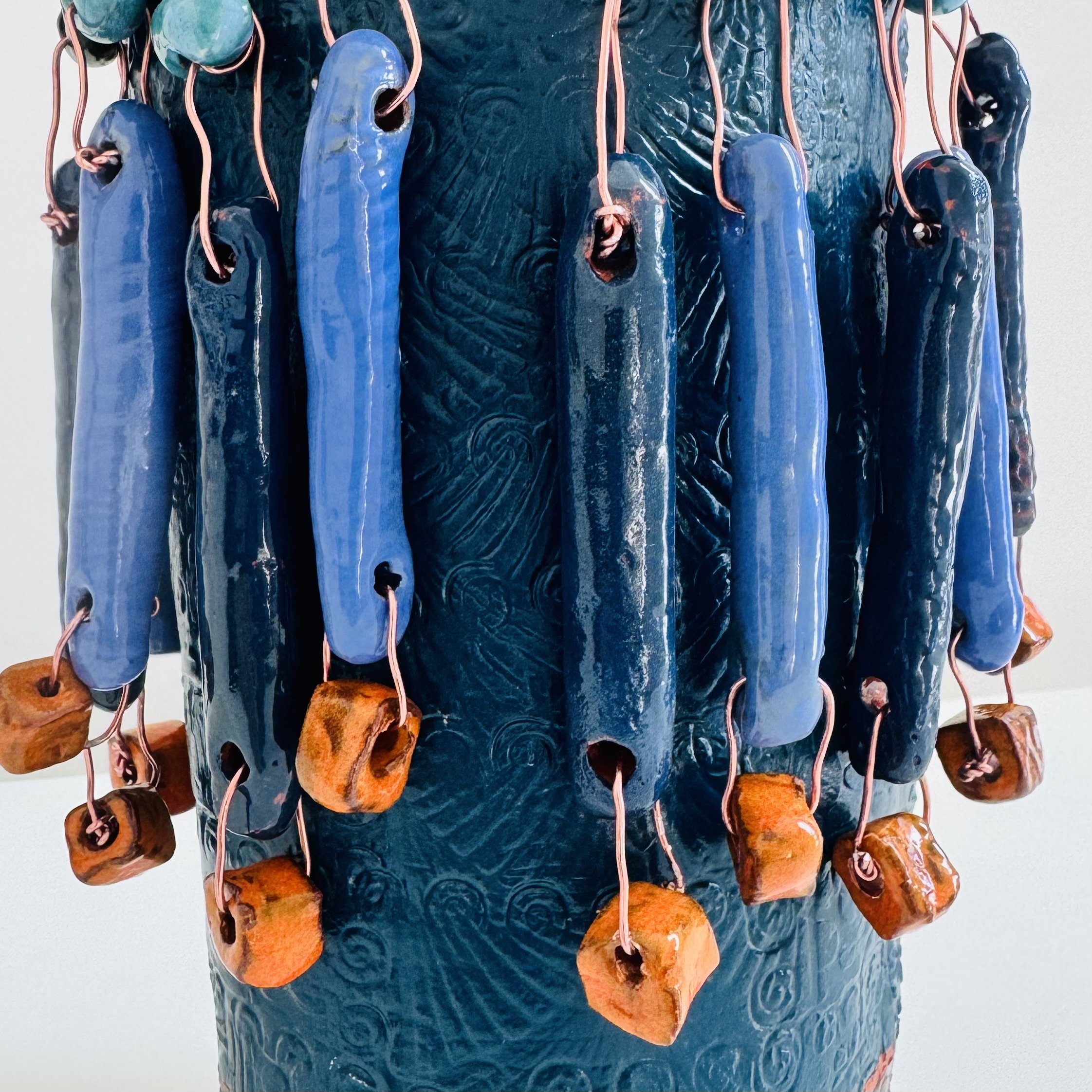 Close detail of a GOBI figure by Brigitte Bouquet, showing a skirt-like layer formed from ceramic pieces in varying shades of blue with orange accents — fragments assembled into something that feels at once ancient and alive.