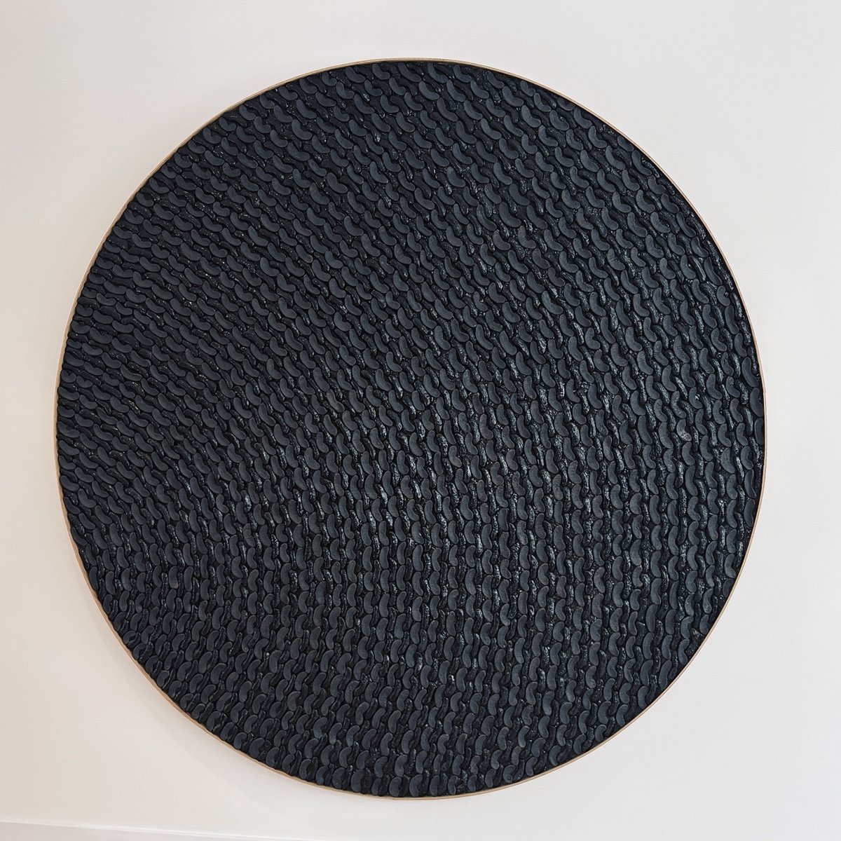 A round black textured mat with small pebble-like bumps, bordered by a thin metallic or gold-colored edge, placed on a white surface.