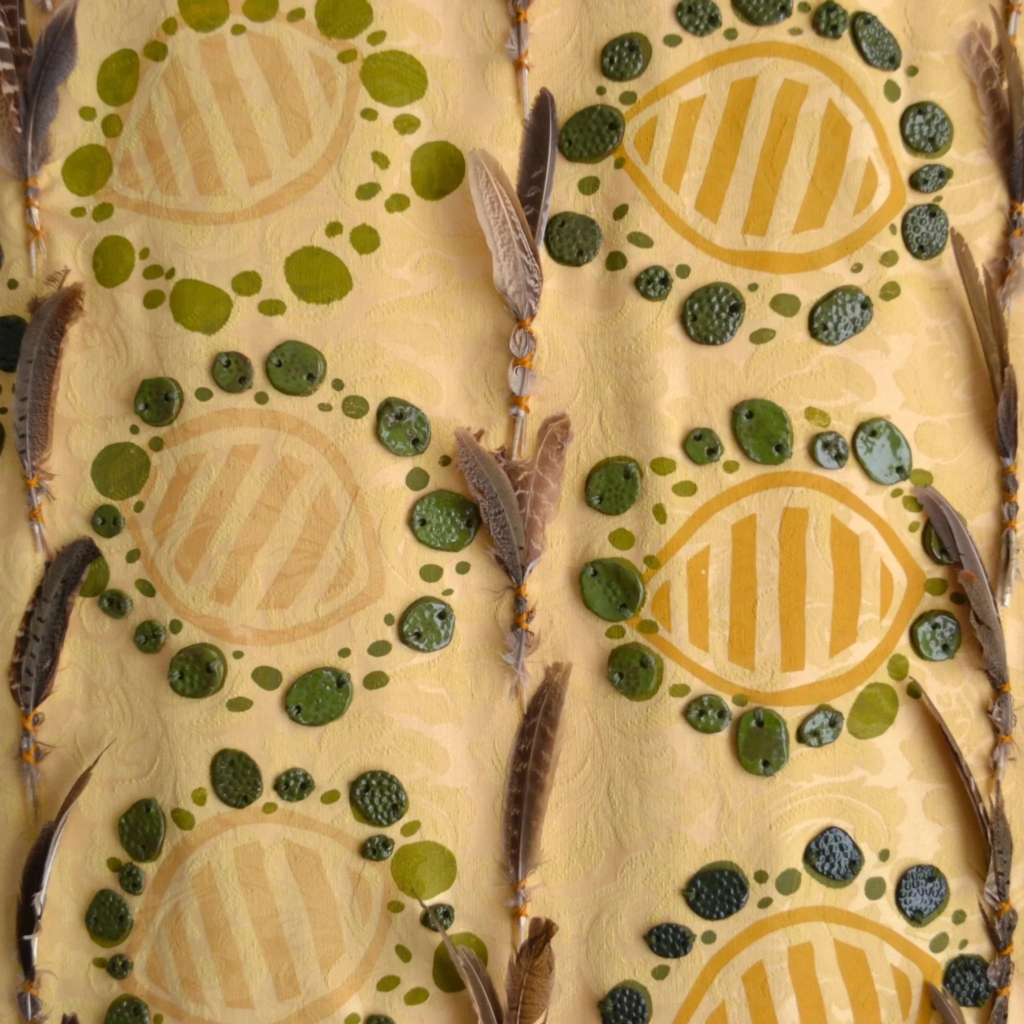 Decorative arrangement of feathers, green beads, and yellow painted design on a yellow fabric background.