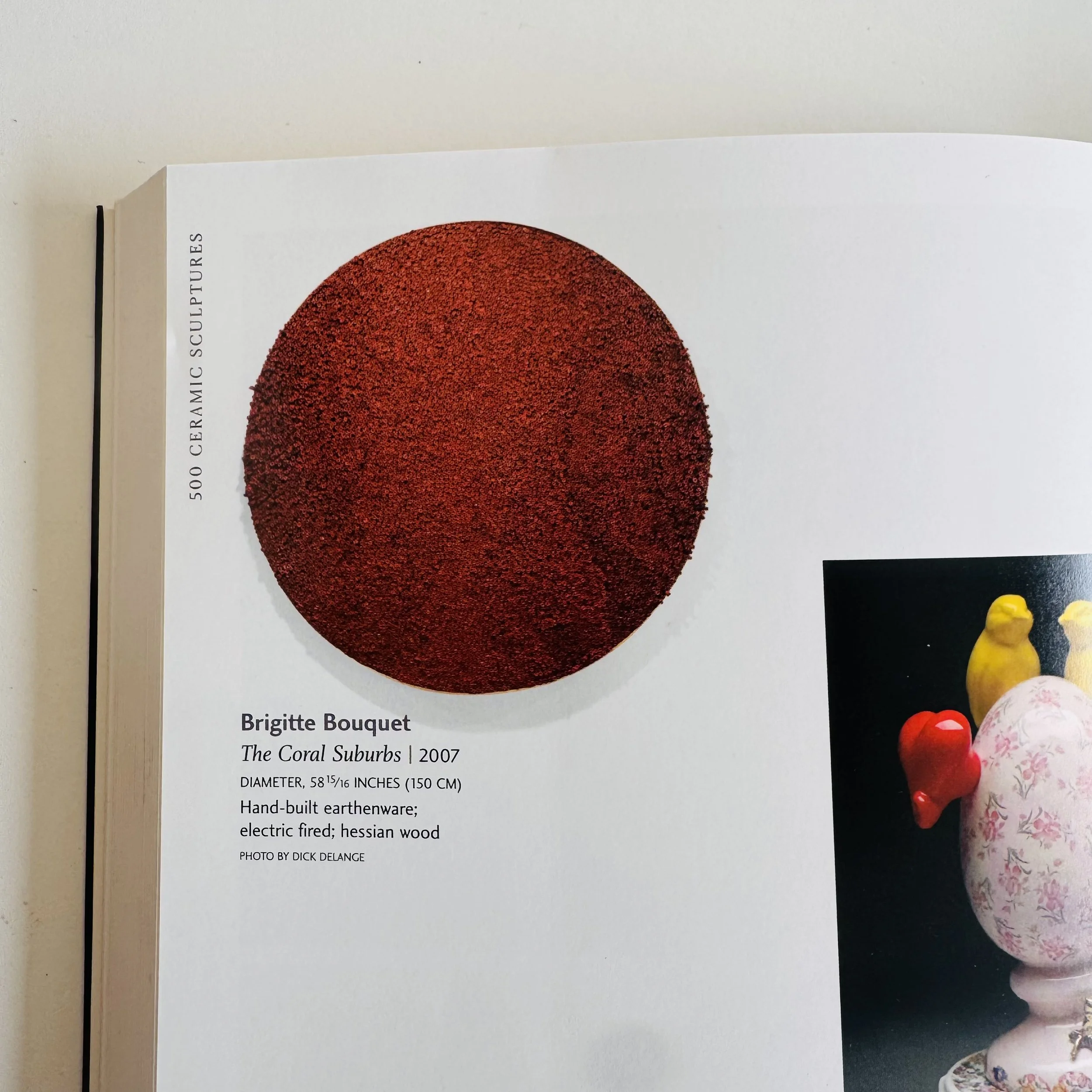 Page from an art book featuring a red ceramic sphere titled 'The Coral Suburbs' by Brigitte Bouquet, 2007, measuring 58 15/16 inches in diameter, made of hand-built earthenware, electric fired, in Hessian wood, with a photo credit to Dick Delange.