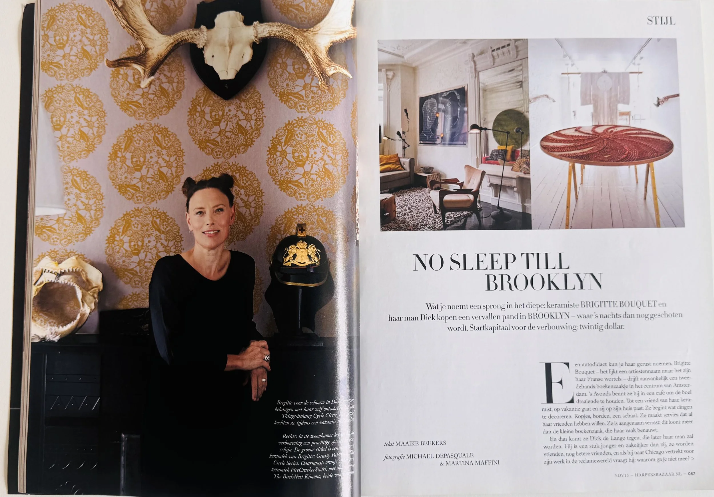 Magazine page with a woman standing in front of a patterned wallpaper wall, a mounted antler skull decoration above her head, and a black and gold handbag on a small table beside her. There are two smaller images of interior design decor and furniture on the right side, along with text in Dutch and English.