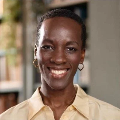 A smiling woman with short hair, wearing a beige shirt and hoop earrings.