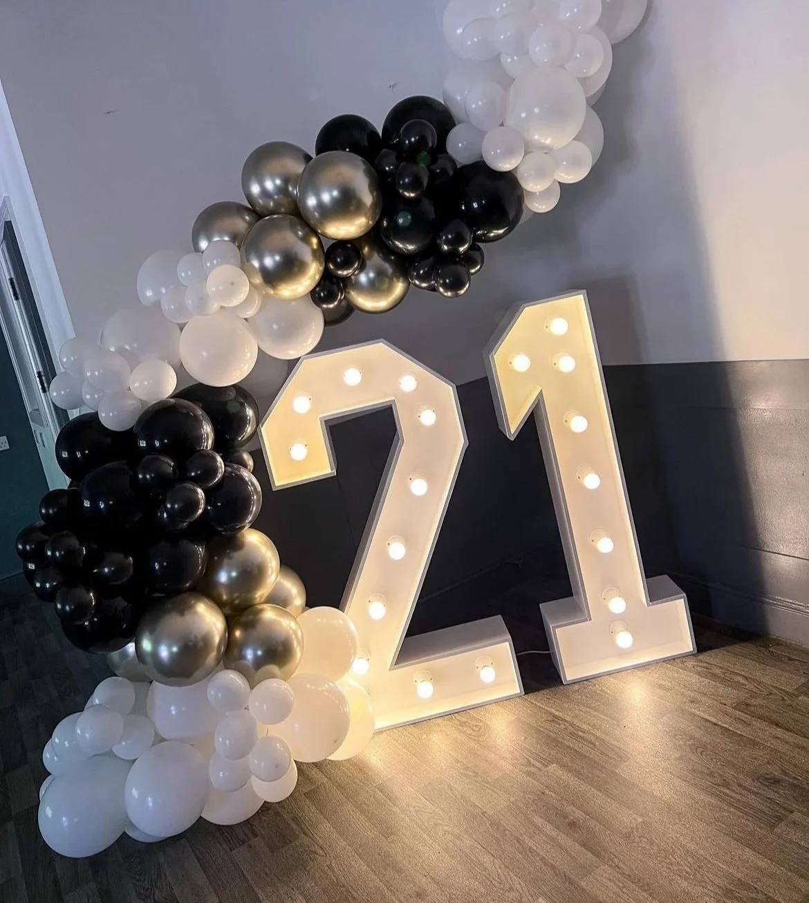 Large illuminated number 21 with black, white, and gold balloons arranged in an arch on top and to the side.