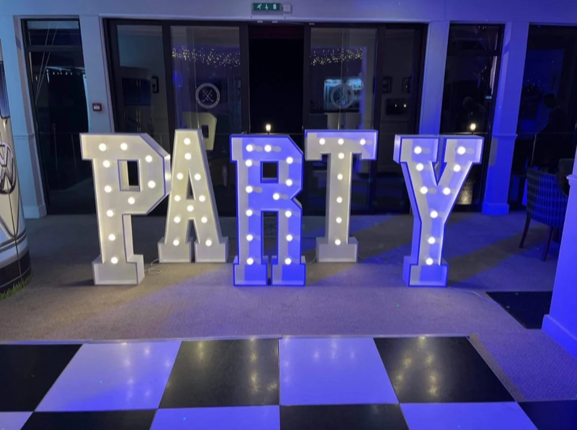 Decorative large illuminated letters spelling 'PARTY' in white and blue lights standing on a dance floor.