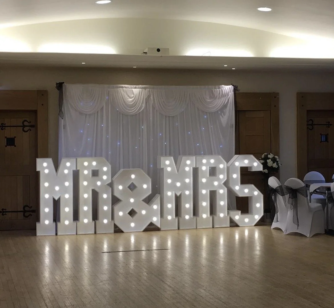 Illuminated wedding or event sign showing the word 'MR & MRS' on a decorated wall.