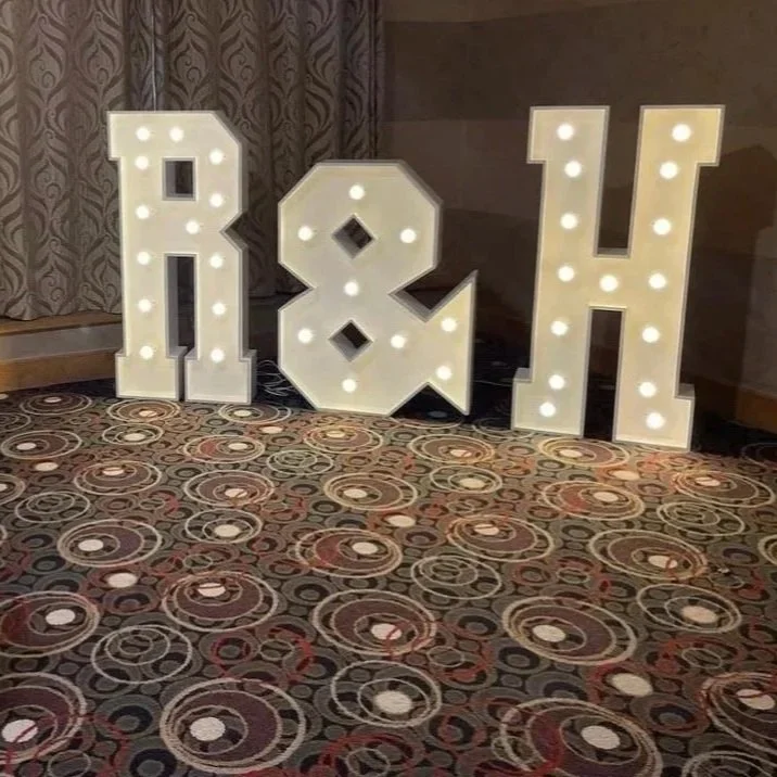 Large white marquee letters spelling 'I & H' with light bulbs on a carpeted floor in front of a curtain backdrop.