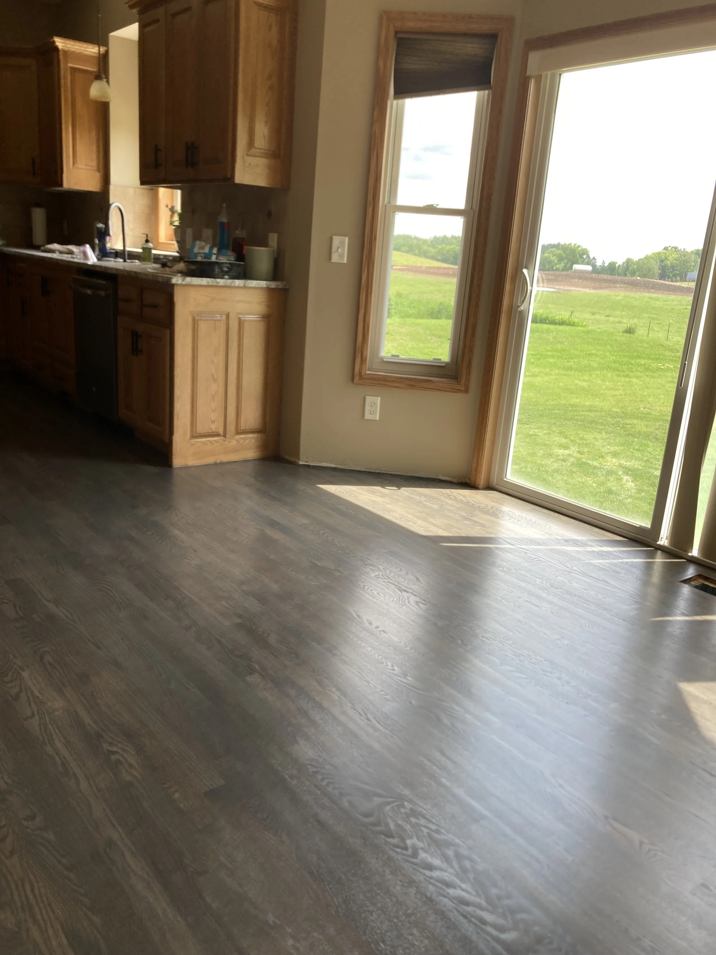 Interior view of a kitchen with wooden cabinets, a stainless steel sink, and large sliding glass doors leading to a grassy outdoor area.