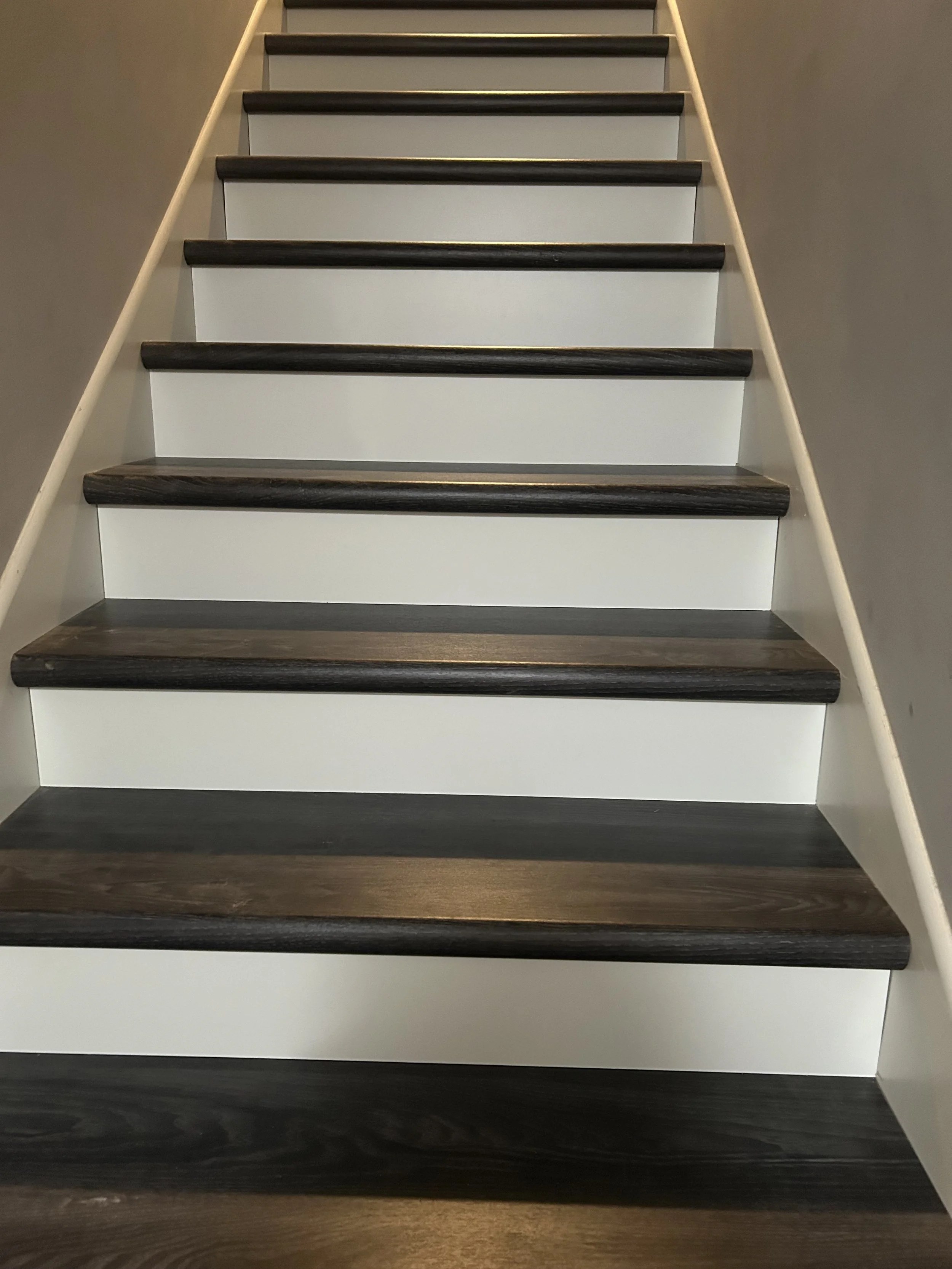 Photo of a staircase with dark wooden steps and white risers, viewed from the bottom looking up.
