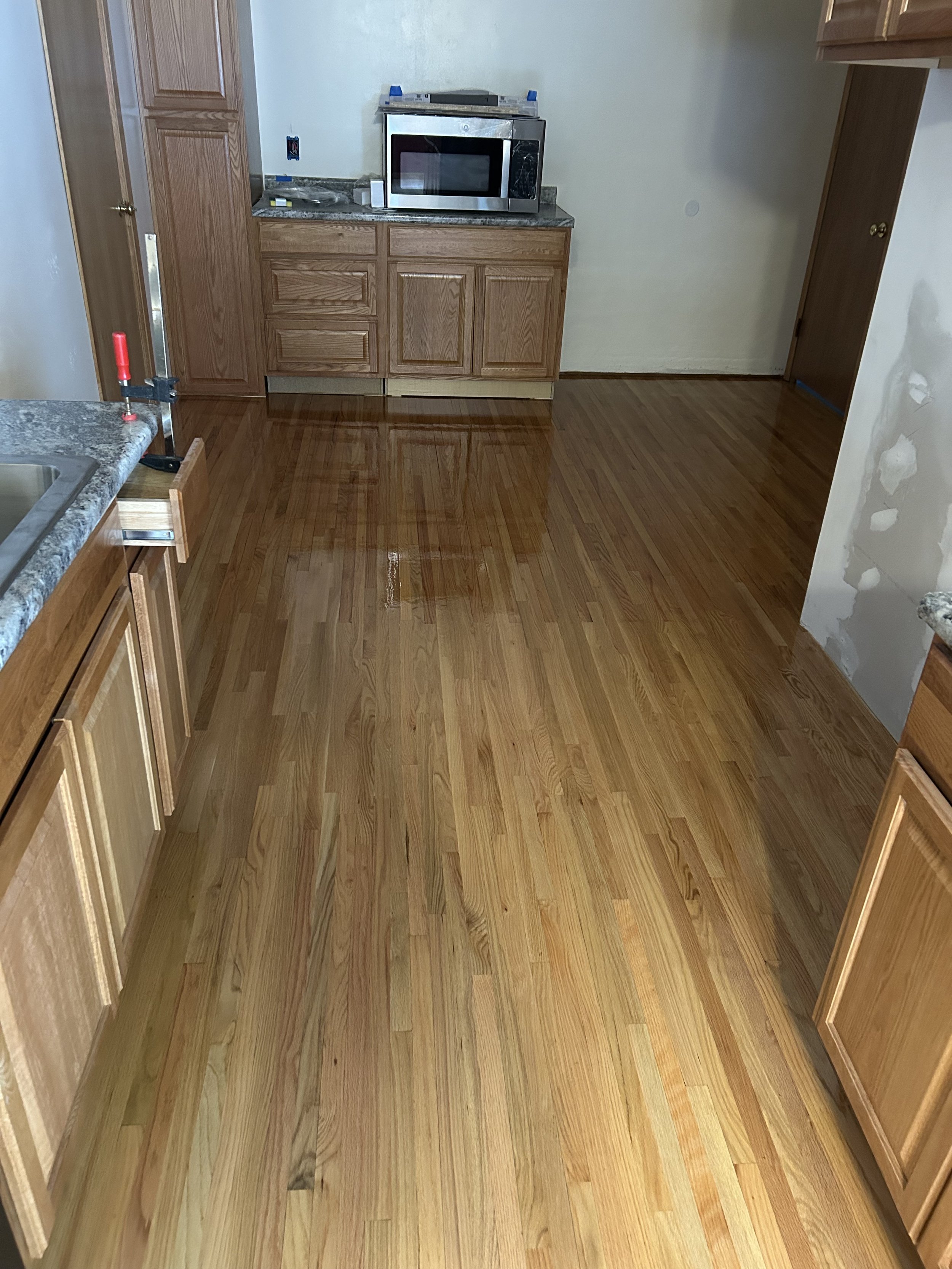 Kitchen with newly installed hardwood floors, natural wood cabinets, granite countertops, and a microwave on the counter.