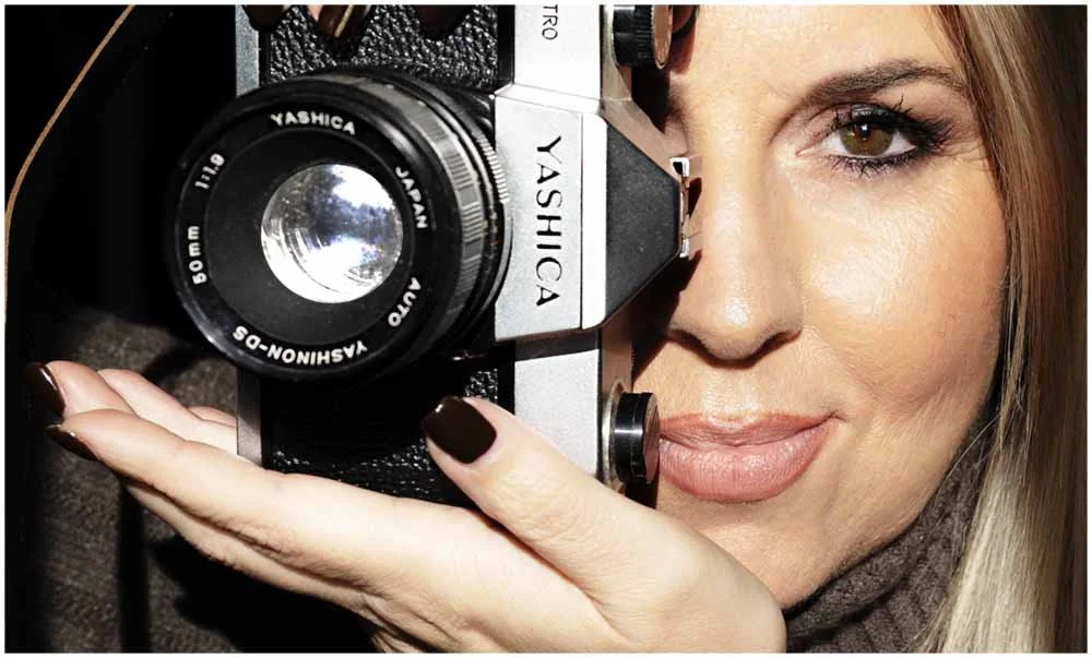 The photographer holding a vintage camera close to her face, looking through the viewfinder.