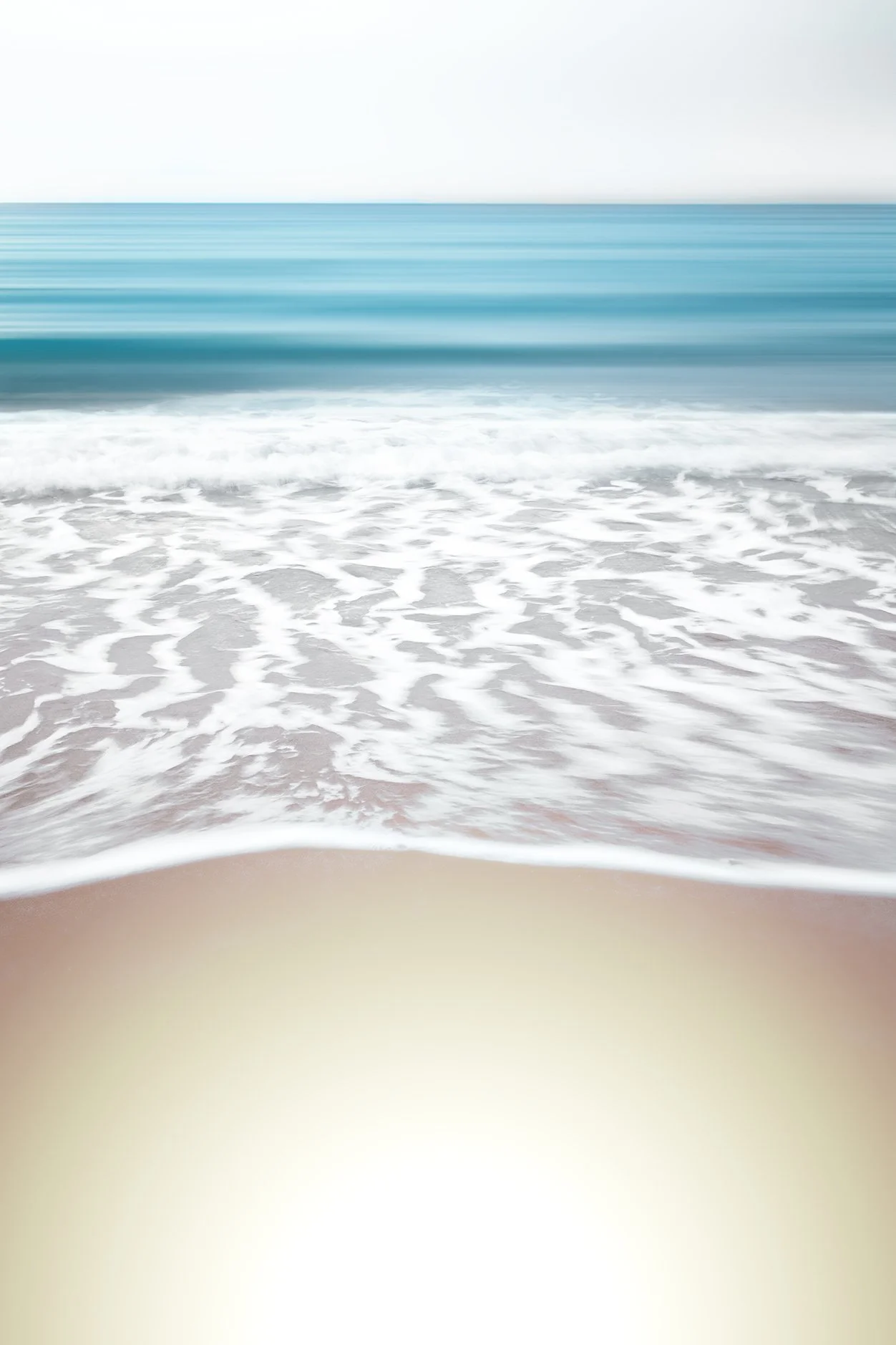 Blurred photo of ocean waves approaching sandy shore with foam and turquoise water.