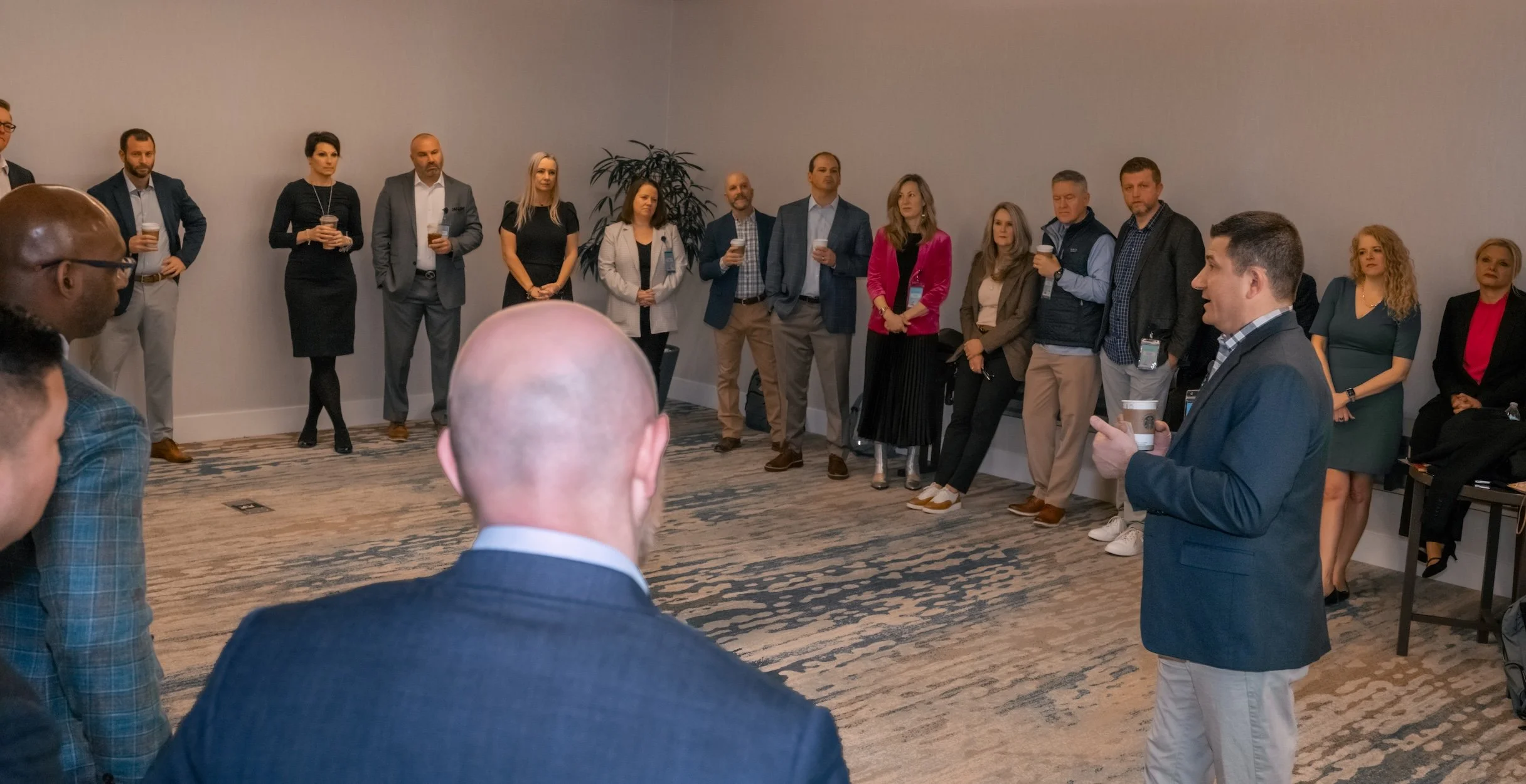 Professional Event Photography by Saint Paul Photographer Jay Cupcake. Man in a blue jacket giving a presentation to a group of people in a conference room, with some holding coffee cups.