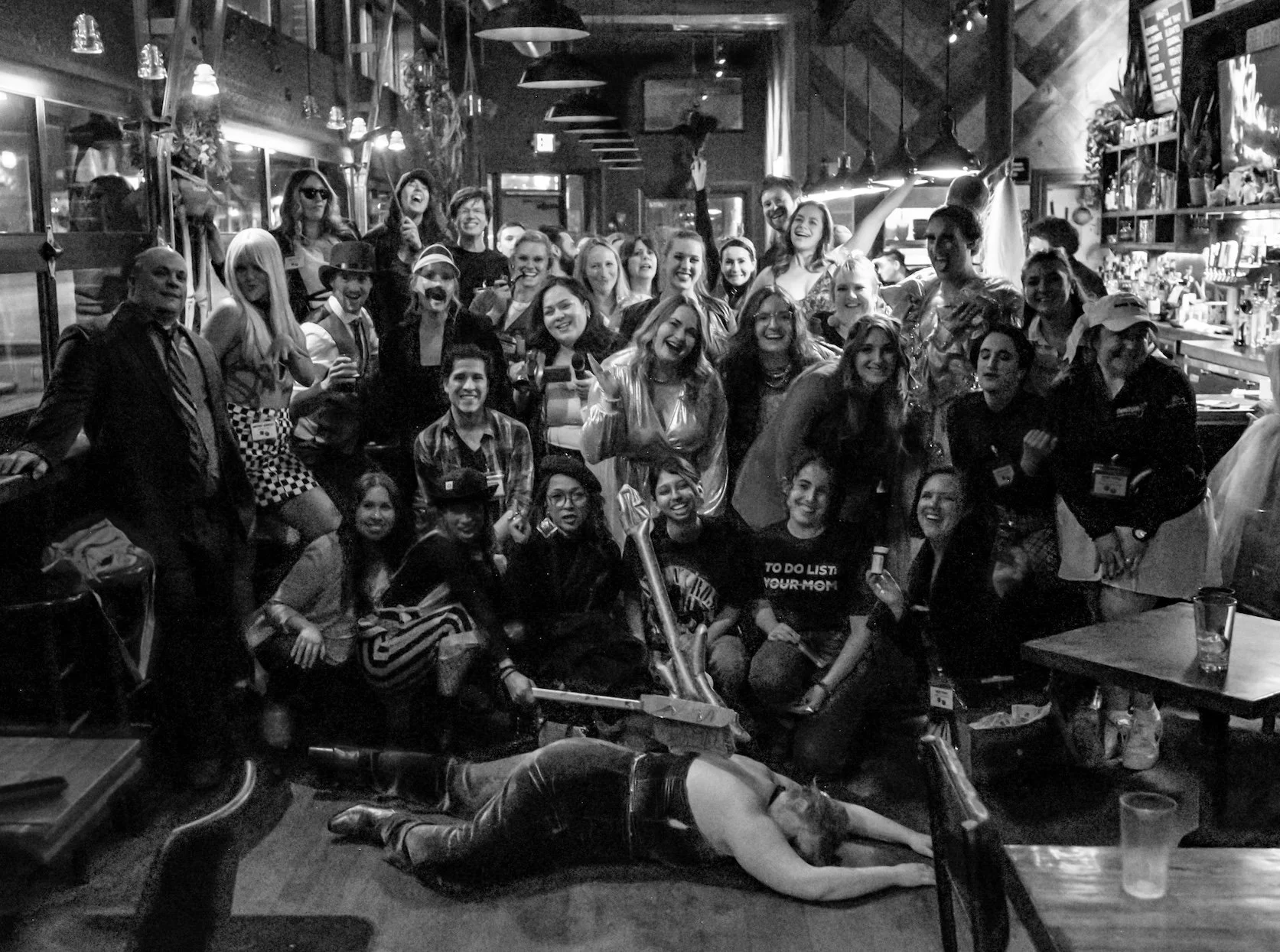 Professional Event Photography by Twin Cities Photographer Jay Cupcake. A large group of people in a bar or restaurant, posing for a photo, with one person lying on the floor in front of the group.