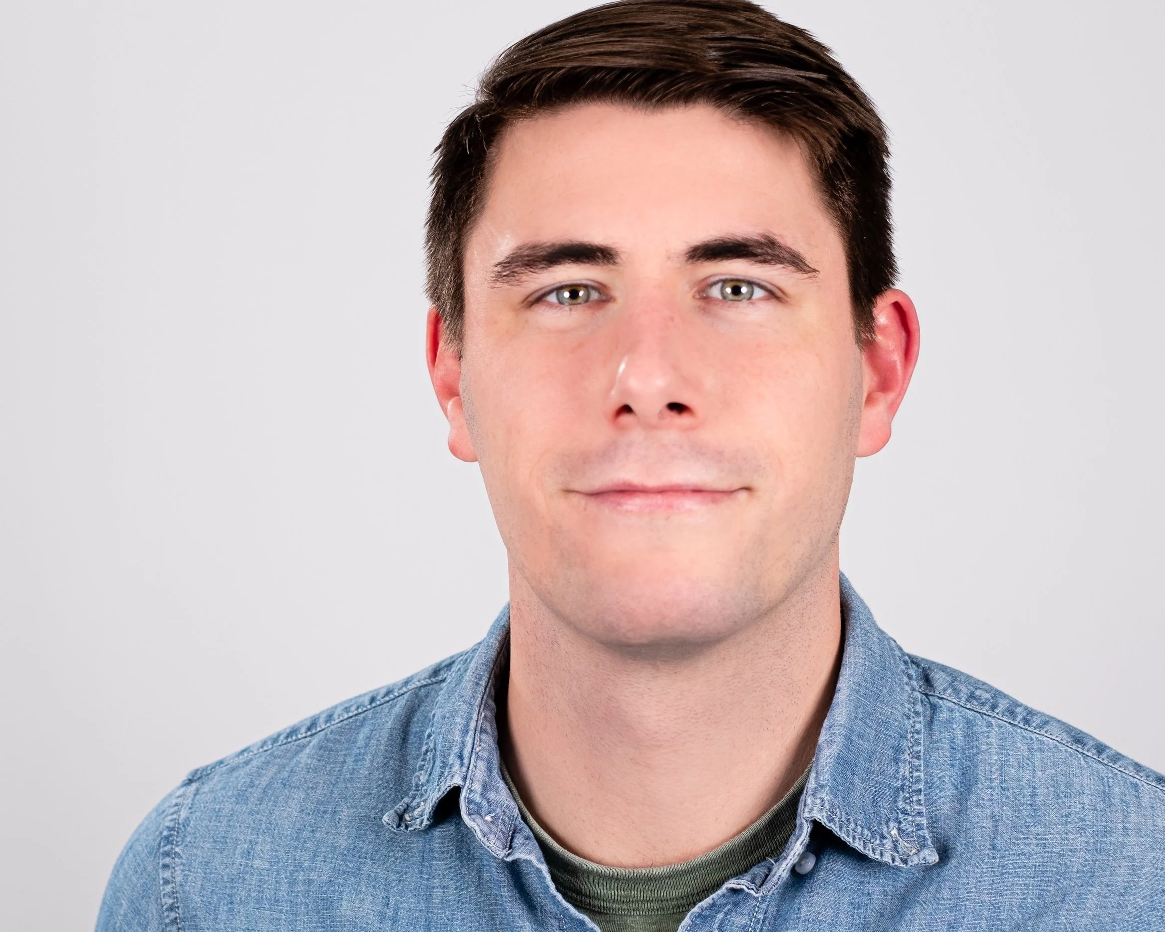 Professional Actor Headshot by Saint Paul Photographer Jay Cupcake. A young man with brown hair, blue eyes, and fair skin, wearing a blue denim shirt, posing against a plain white background.