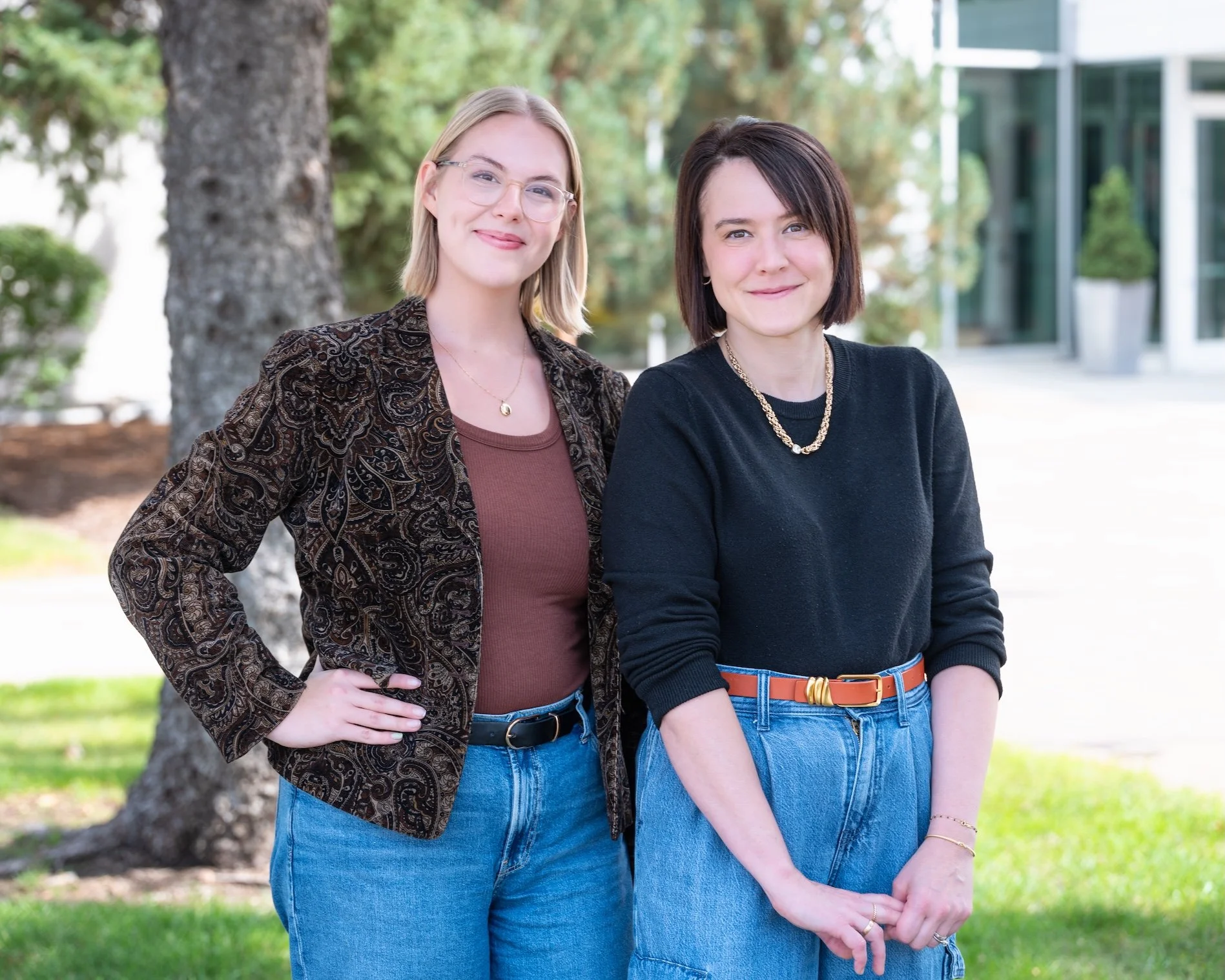 Professional Portrait Photography by Twin Cities Photographer Jay Cupcake. Two women standing outdoors near a tree, smiling at the camera, with a building in the background.