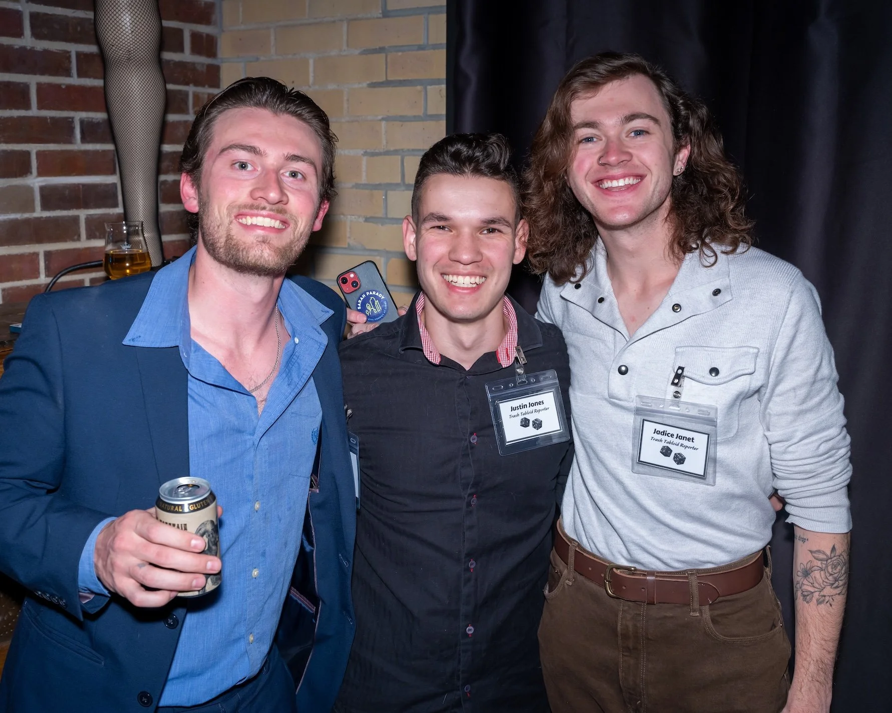 Professional Event Photography by Twin Cities Photographer Jay Cupcake. Three men smiling, standing close together at an indoor event. The man on the left wears a blue blazer and holds a canned beverage. The man on the right has a tattoo on his left 