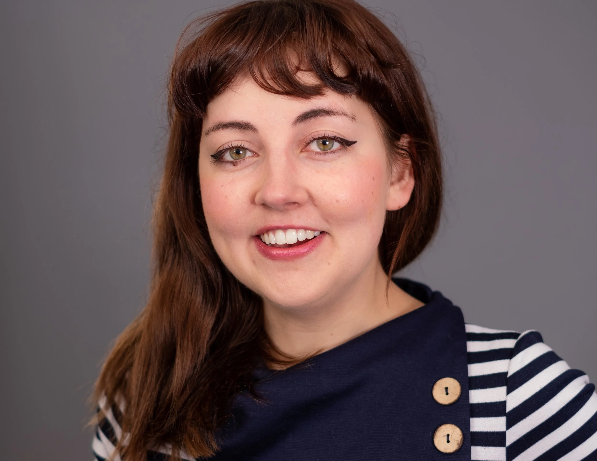 Professional Actor Headshot by Minneapolis Photographer Jay Cupcake. A woman with shoulder-length brown hair wearing a striped navy and white top, smiling against a gray background.